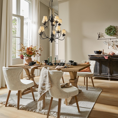Esszimmer mit Holztisch, cremefarbenen Polsterstühlen, Blumen und schwarzem Kronleuchter