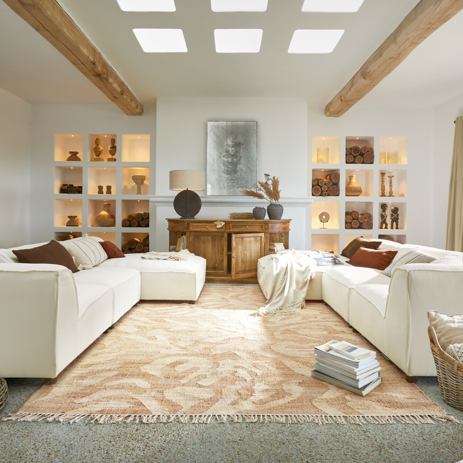 Gemütliches Wohnzimmer mit weissem Sofa, Holzkommode und beigem Teppich mit Pflanzenmuster, Holzdekorationen