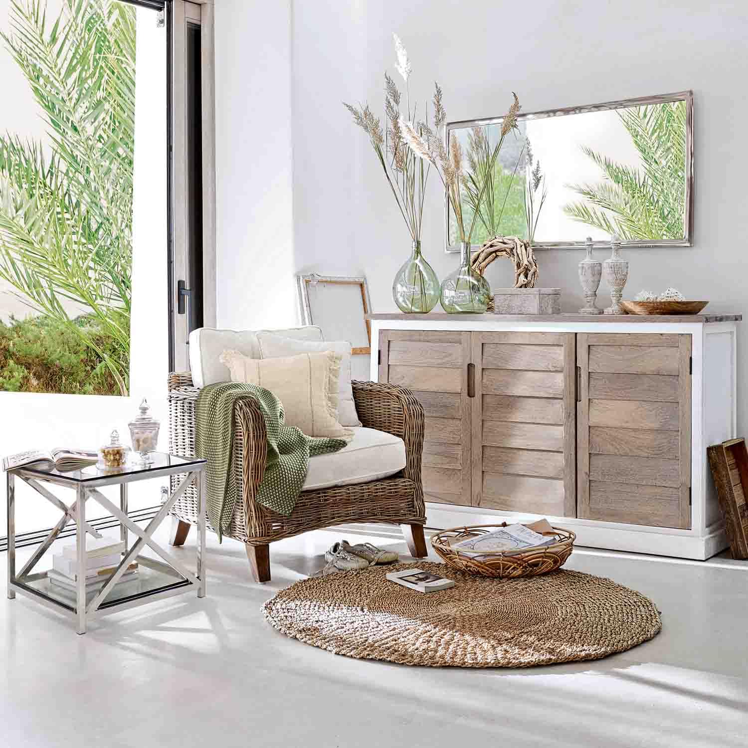 Helles Wohnzimmer mit Korbsessel, Sideboard aus hellem Holz und rundem Naturteppich in gemütlicher Atmosphäre