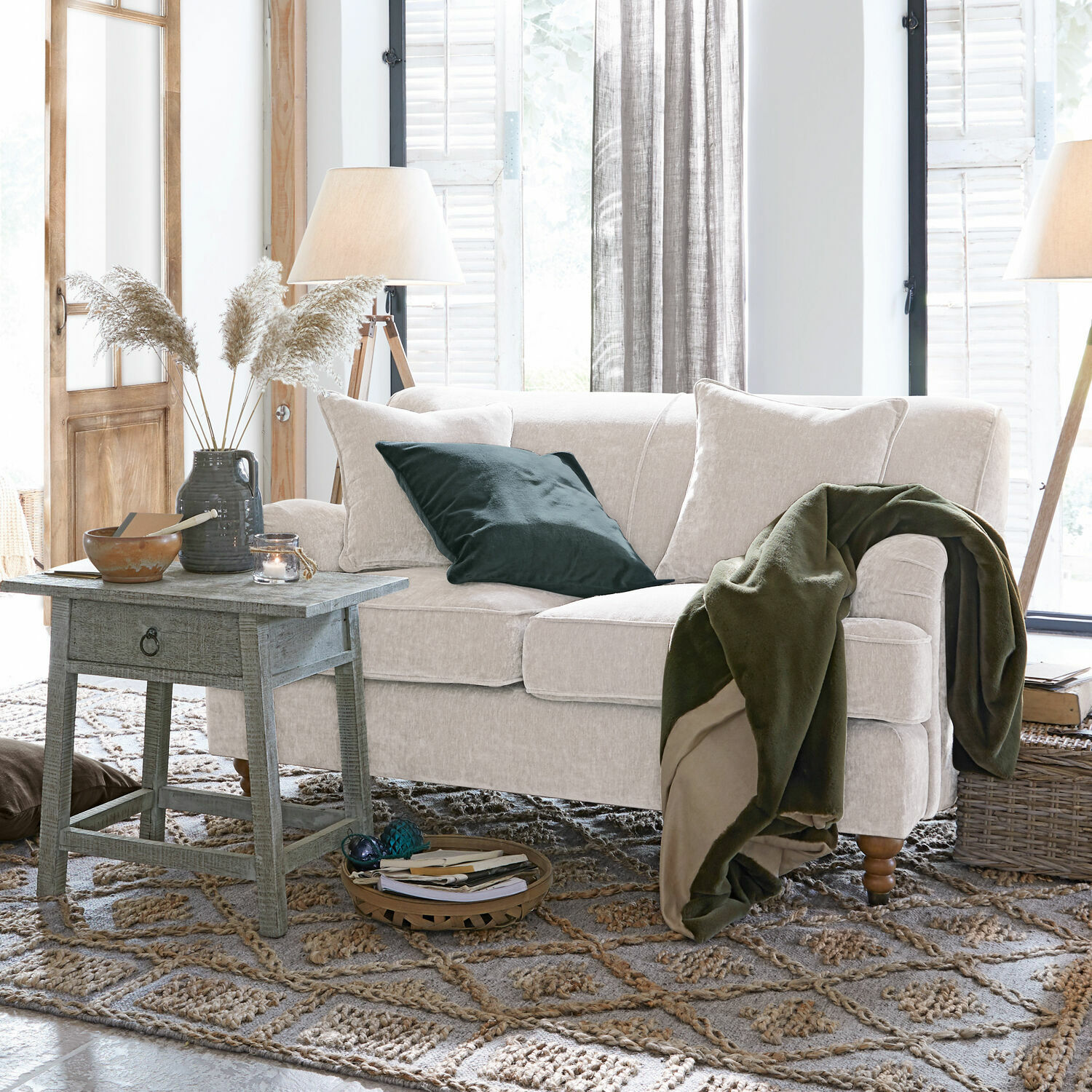 Beiges Sofa aus weichem Stoff mit grünem Überwurf und Kissen in einem gemütlichen Wohnzimmer mit Holztisch