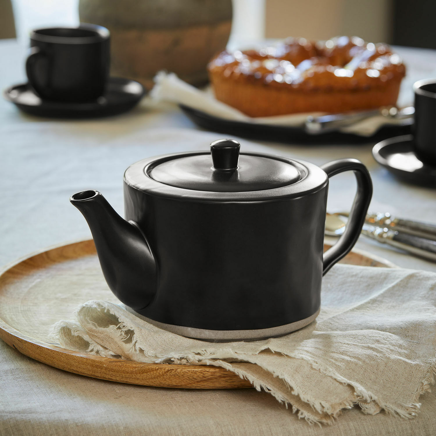 Teekanne Biarré Schwarze Keramik-Teekanne auf Holztisch mit Blumen und Glasflaschen als Dekoration
