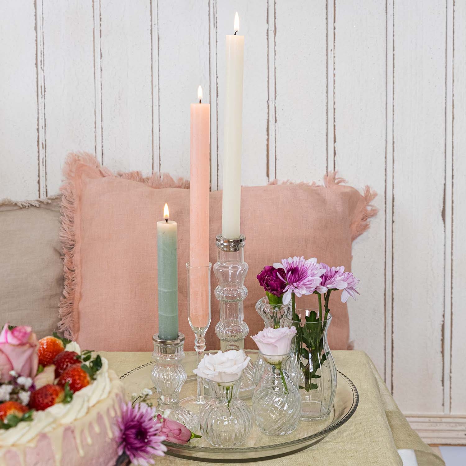 Pastellfarbige Kerzen und kleine Glasvasen mit Blumen auf einem Glastablett auf dem Tisch
