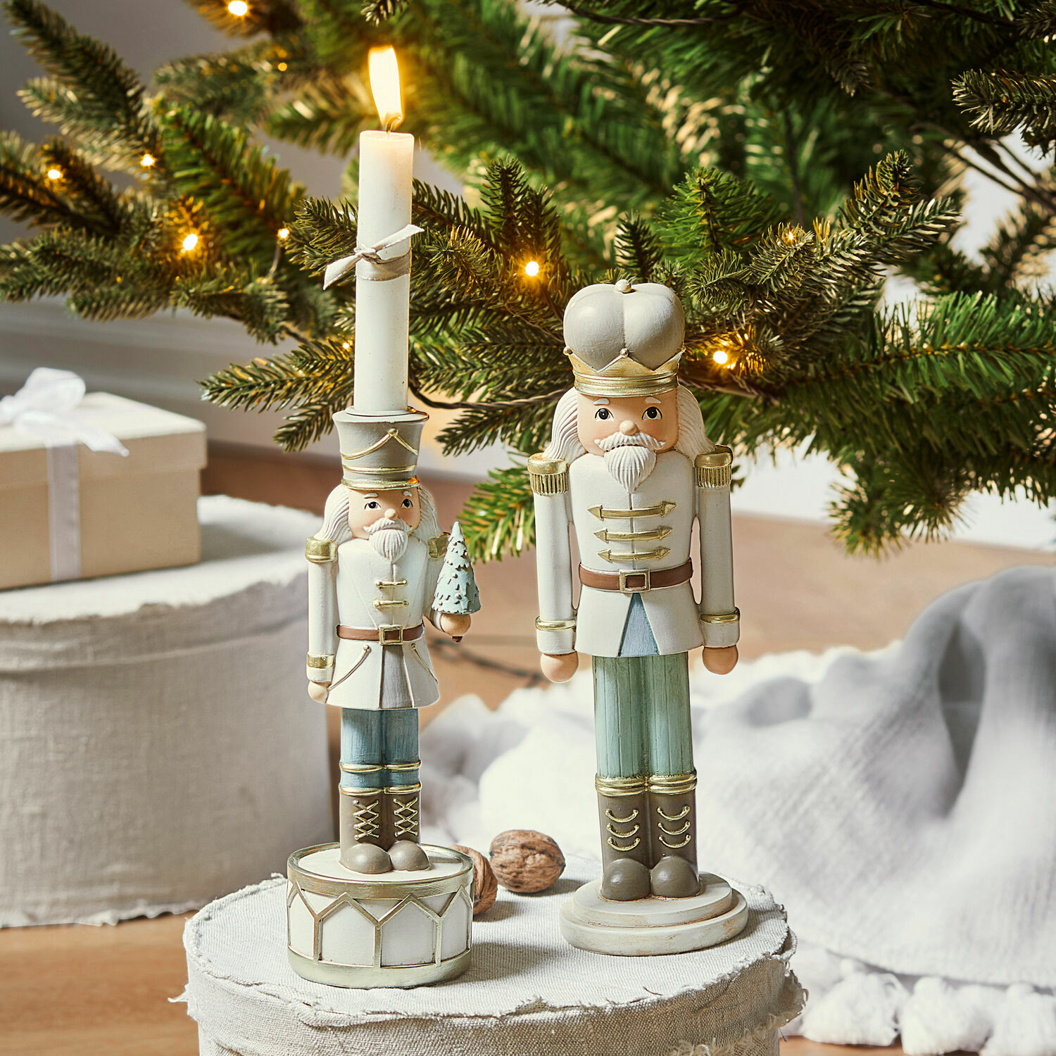 Deko-Nussknacker mit Kerzenständer Ellicott Zwei weisse und grüne Holz-Nussknackerfiguren vor weihnachtlich beleuchtetem Tannenzweig