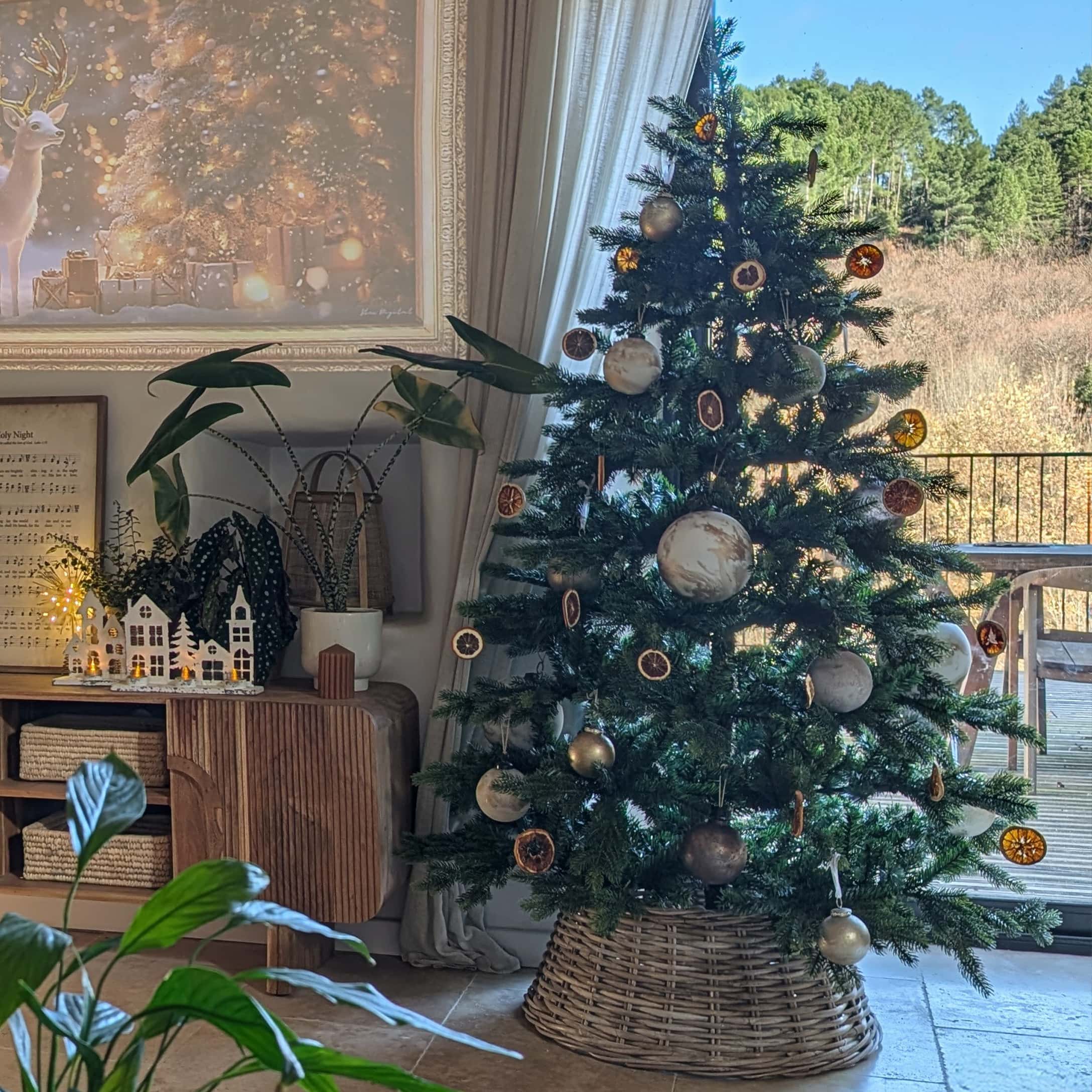 Weihnachtsbaum im Weidenkorb mit natürlichen Anhängern und hellen Kugeln in gemütlichem Raum