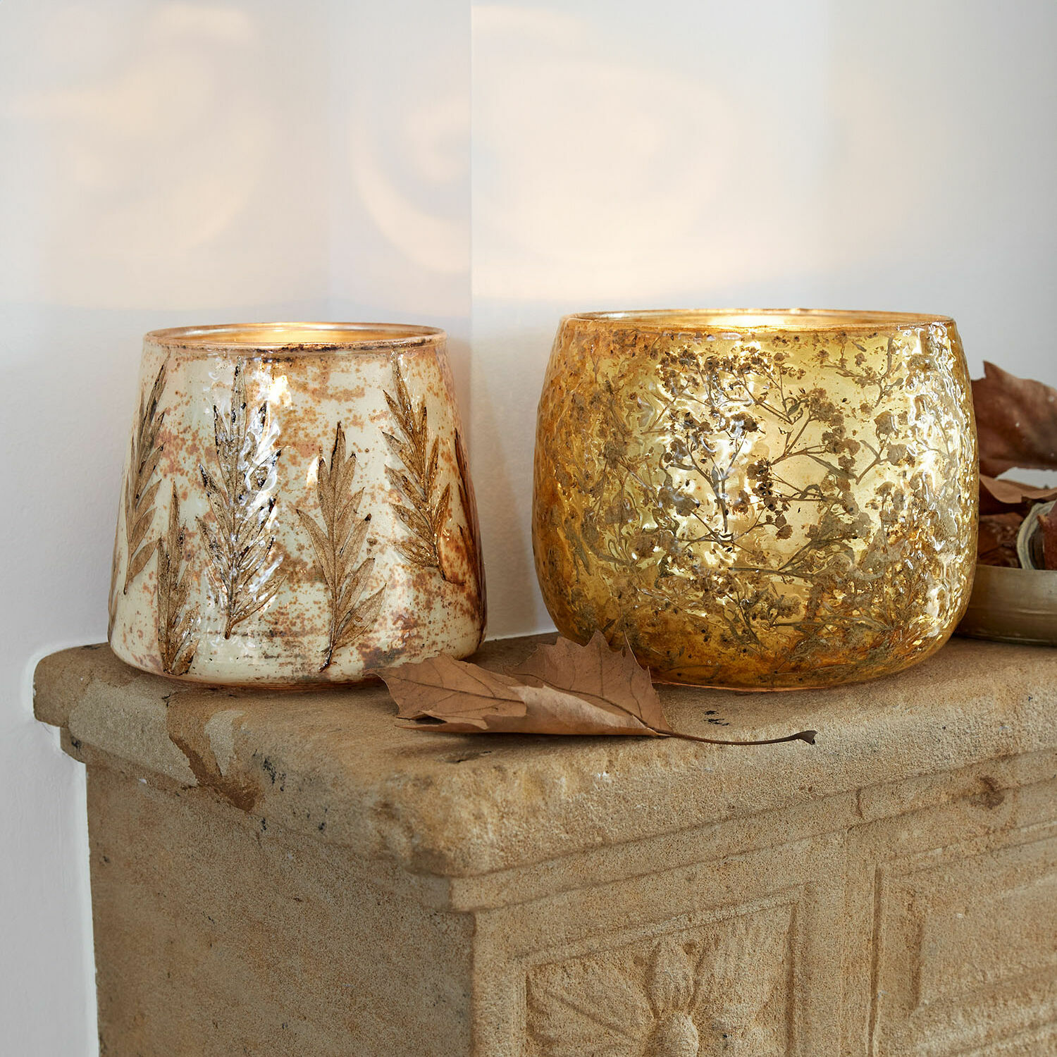 Windlicht 2er Set Hivalen Zwei dekorative Glaswindlichter mit Blattmotiv in Gold und Creme auf steinerner Ablage.