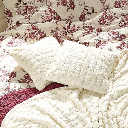Weiche, cremefarbene Plüschkissen und Decke auf Bett mit bordeauxrotem Blumenmuster