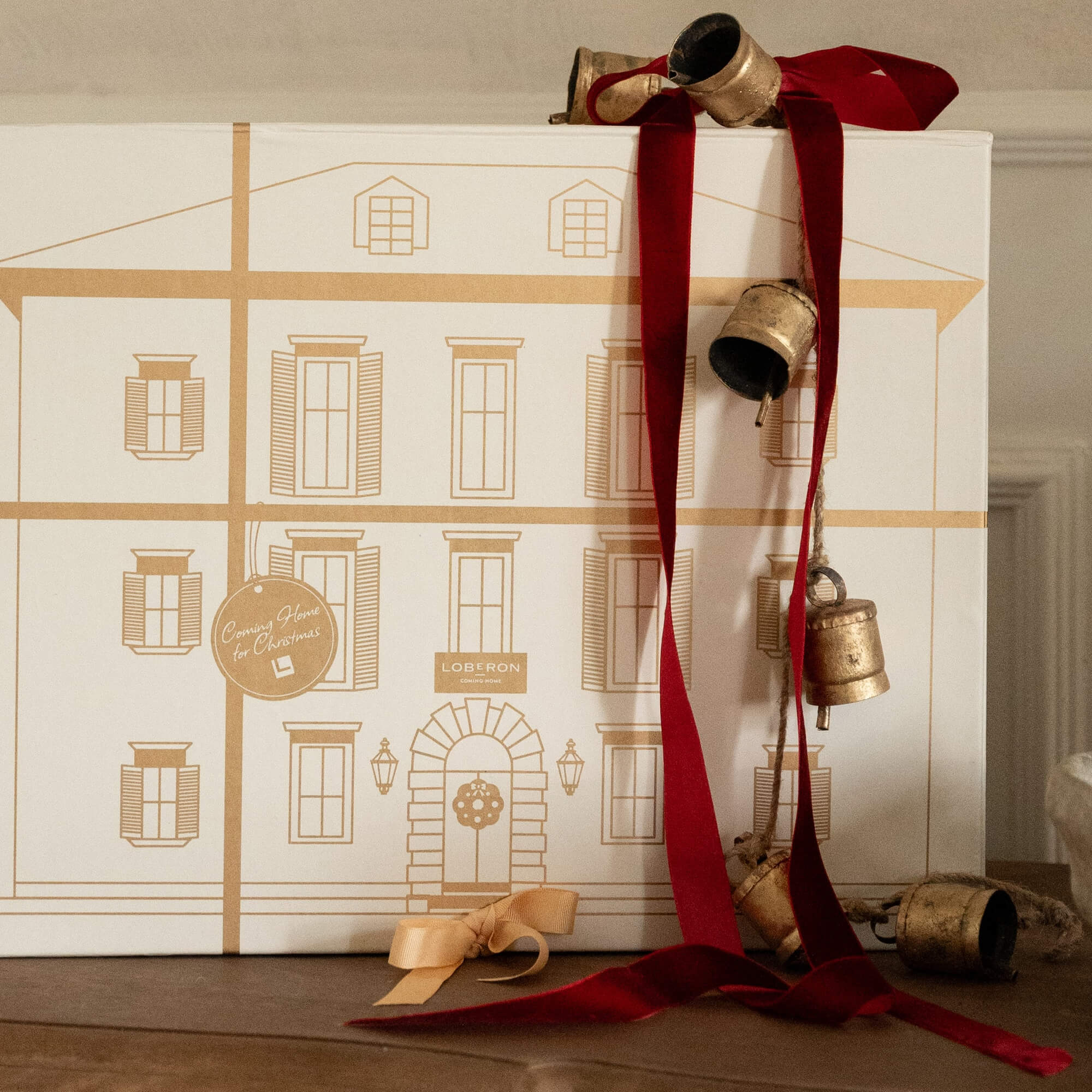 Weihnachtliche Dekoration mit roten Bändern und goldenen Glocken vor weissem Hintergrund mit Hauszeichnung