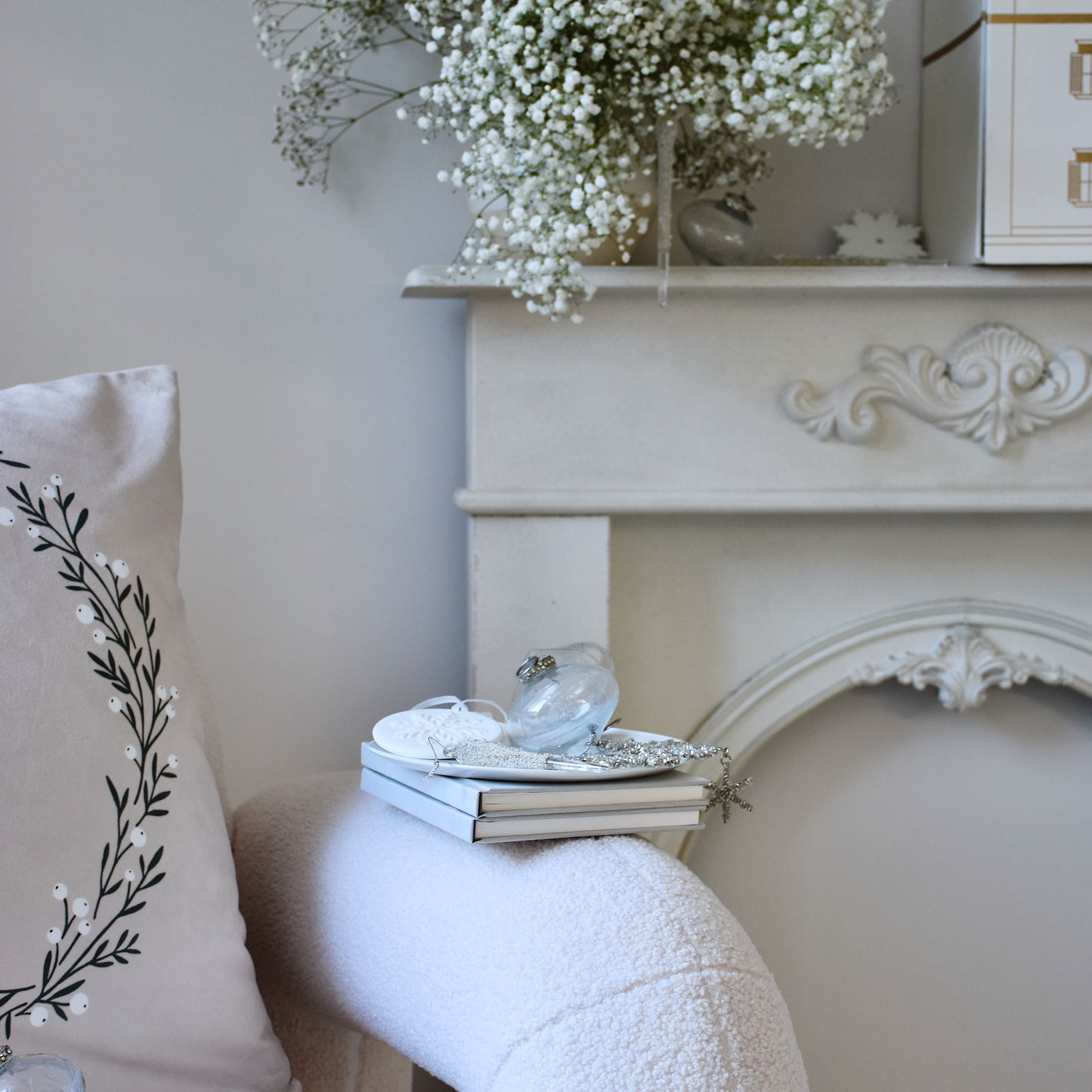 Weisse dekorative Kaminkonsole mit Blumen und Büchern auf weichem Sessel in hellem Zimmer