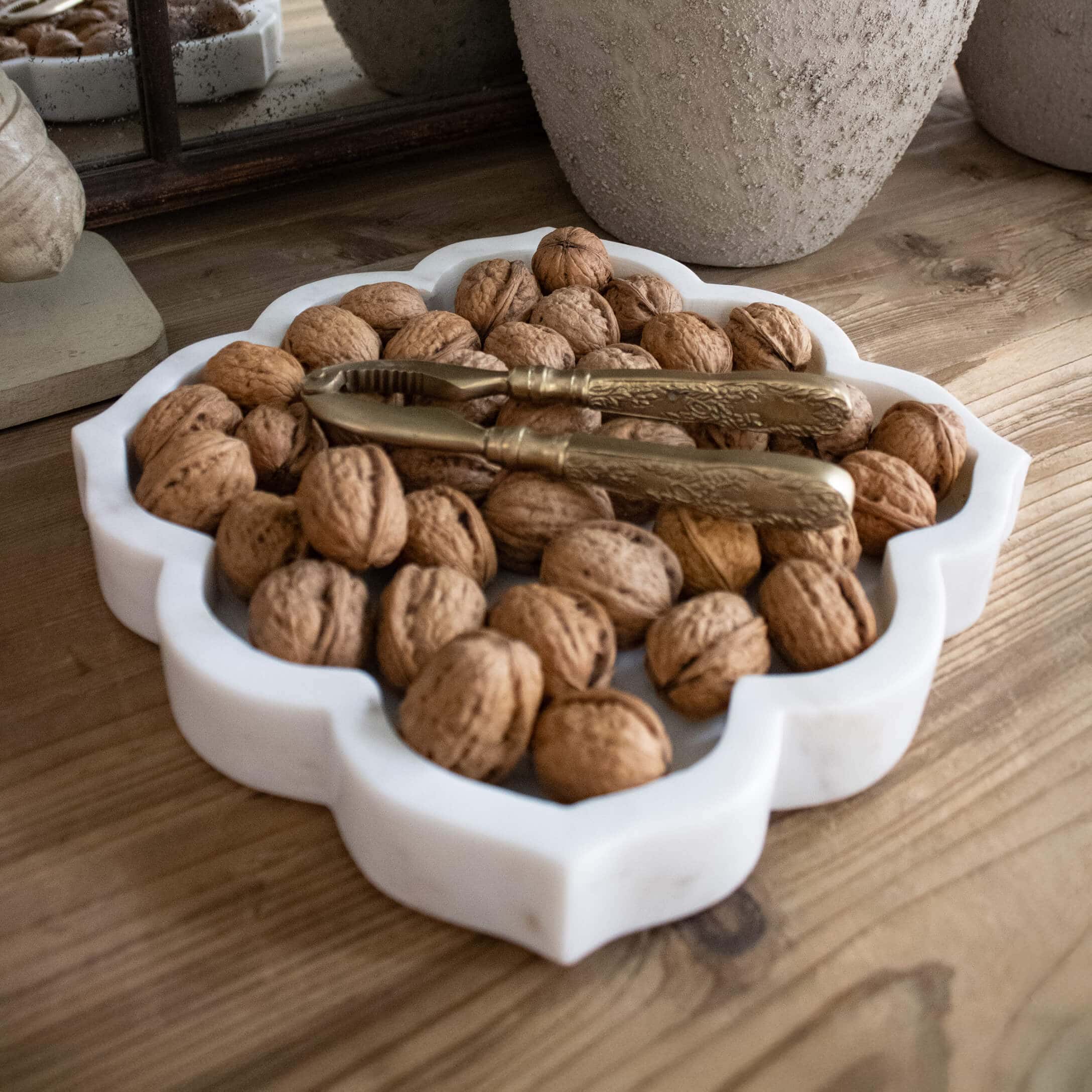 Weisse Marmorplatte mit Walnüssen und goldenem Nussknacker auf Holztisch