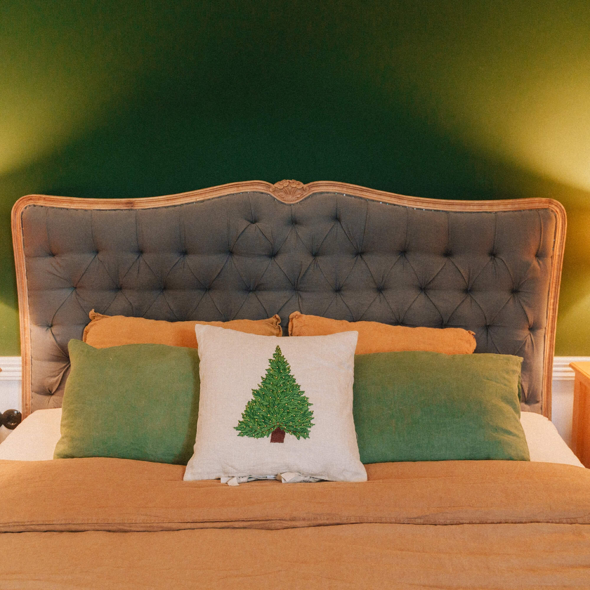 Schlafzimmer mit grauem, gepolstertem Kopfteil sowie grünen und orangefarbenen Kissen, weihnachtliche Dekoration