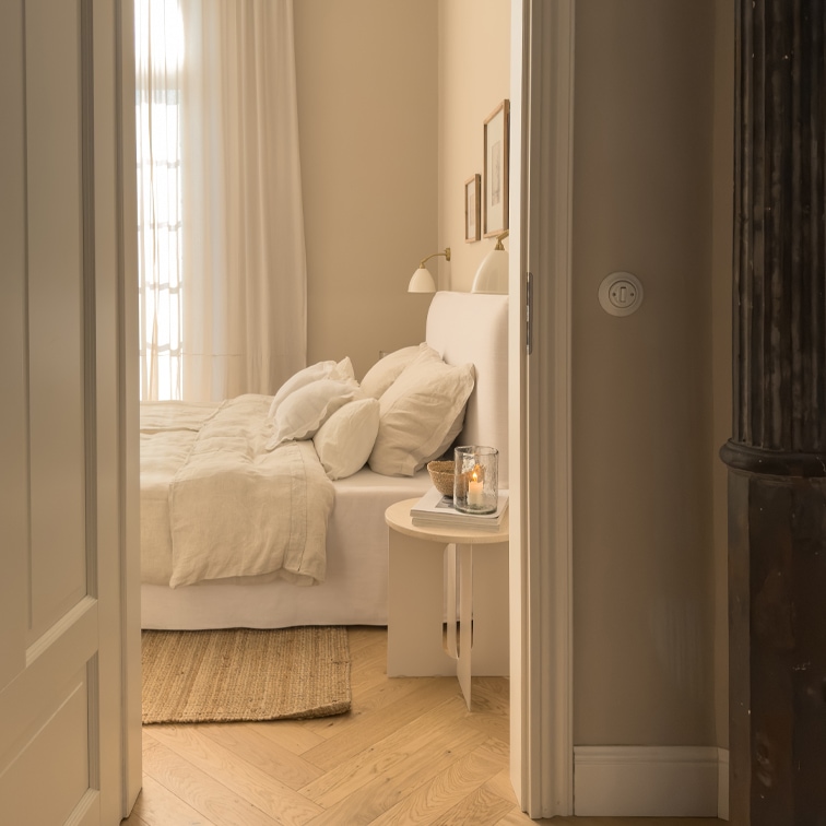 Gemütliches Schlafzimmer in hellen Beigetönen mit Bett und Naturteppich auf hellem Holzfussboden