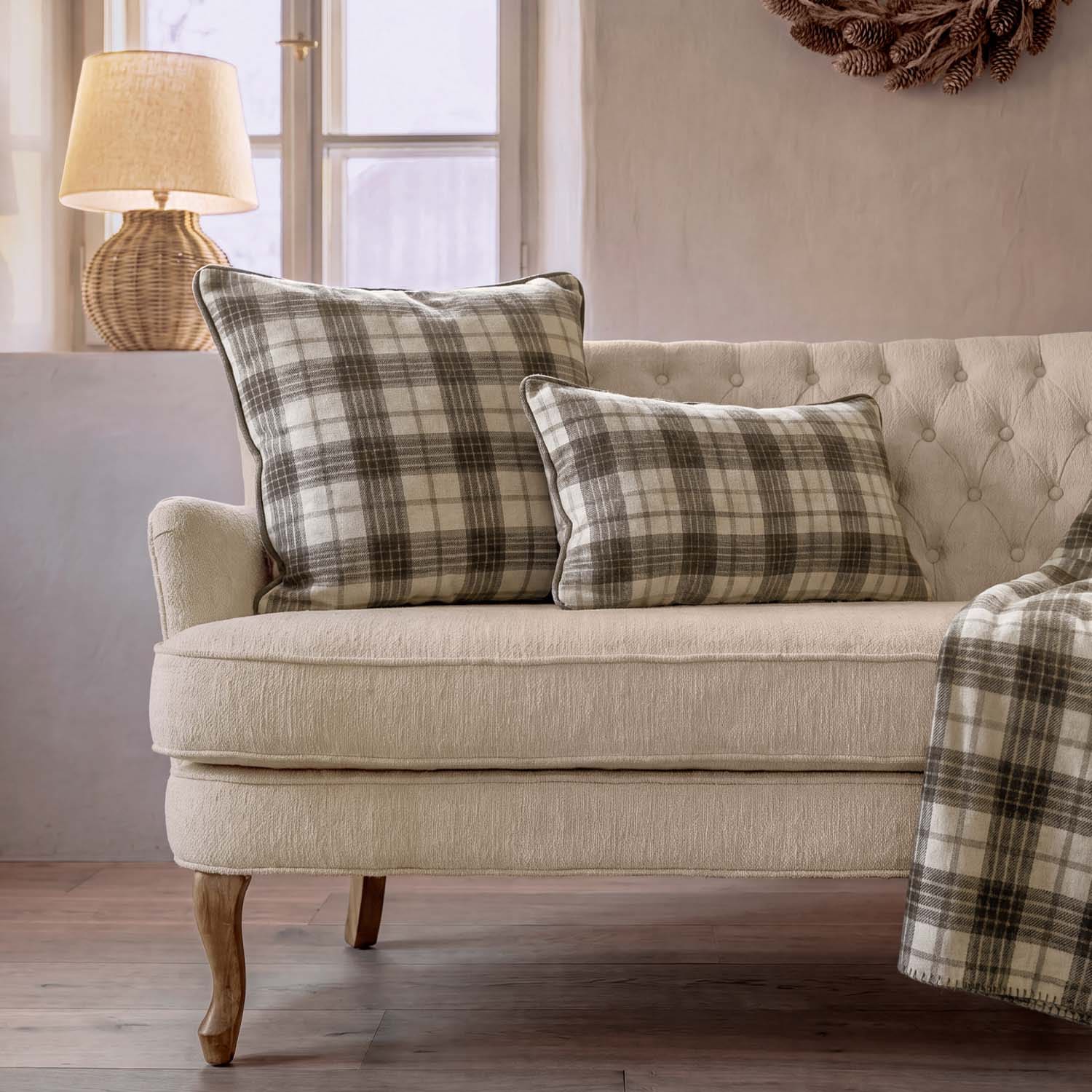 Beiges Sofa mit zwei karierten Kissen in Grau und Creme sowie Lampe vor Fenster im Wohnzimmer