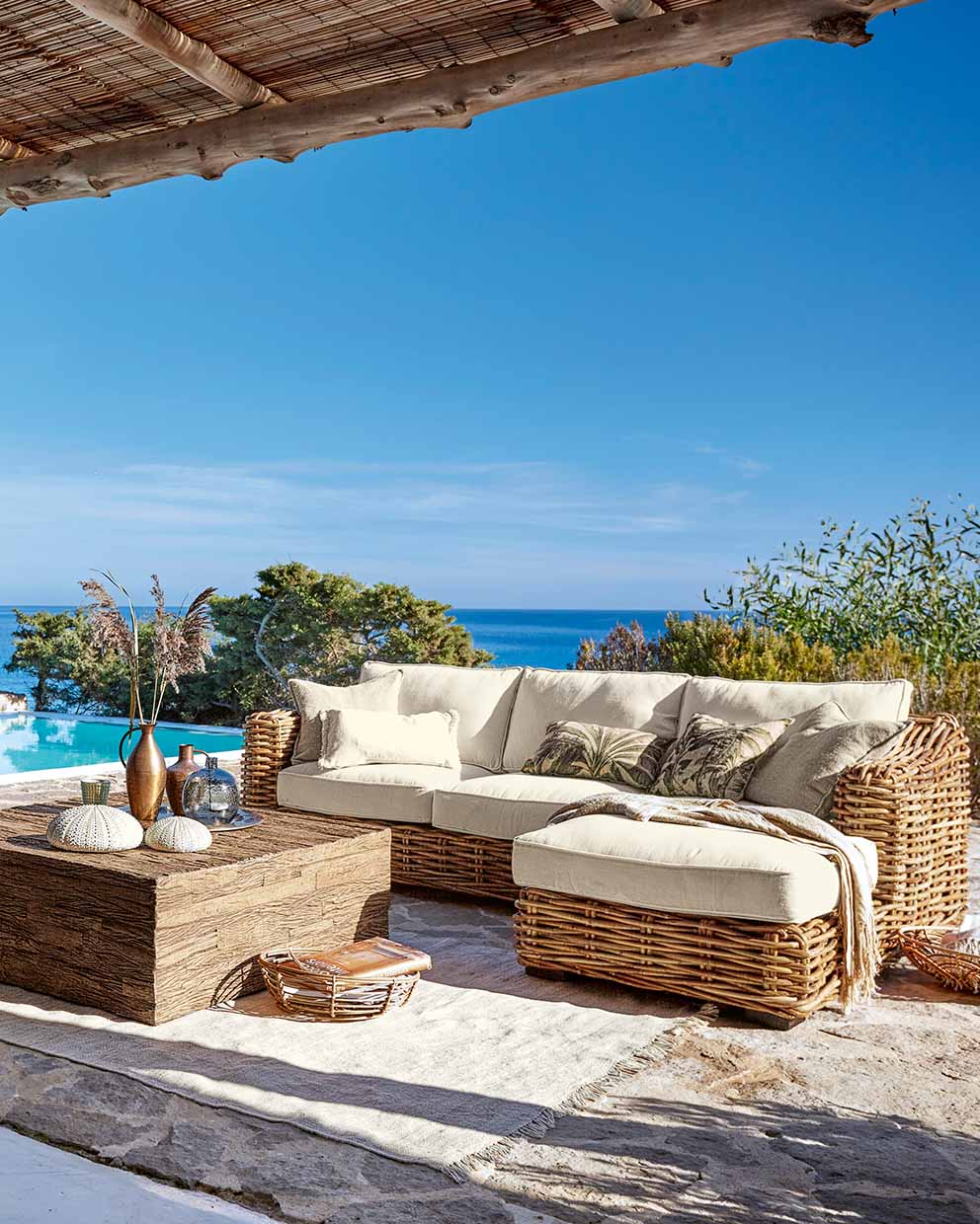Rattan-Gartenmöbel mit cremefarbenen Polstern und Holztisch auf Terrasse mit Meerblick