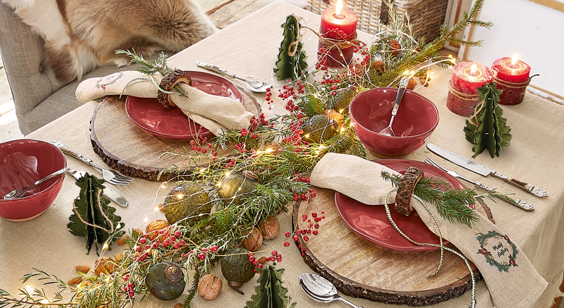 Weihnachtlich gedeckter Tisch mit roten Keramiktellern, Naturdekorationen und brennenden Kerzen