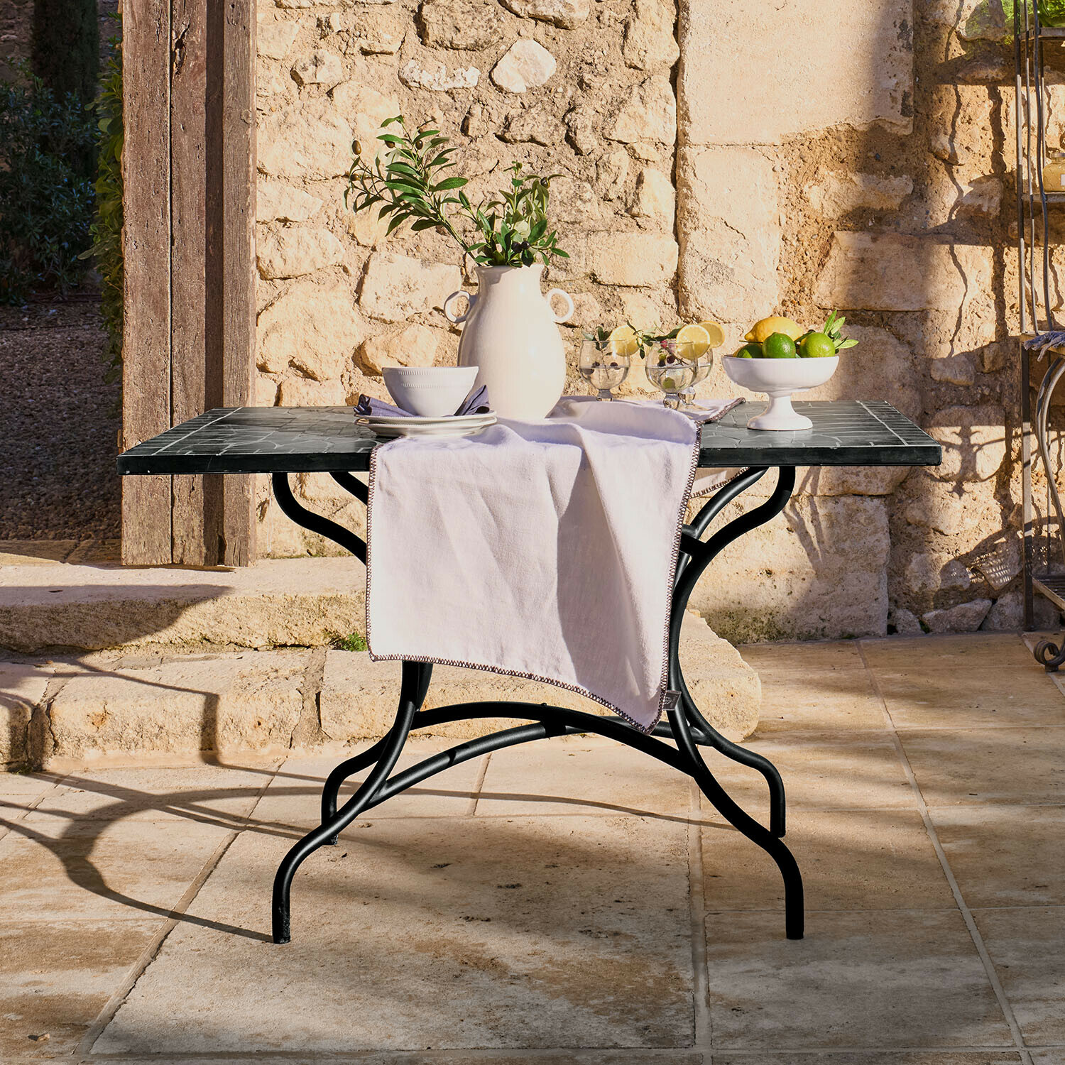 Tisch Maurelle Gartentisch mit schwarzem Metallgestell und Marmorplatte, dekoriert mit weissem Krug und Früchten