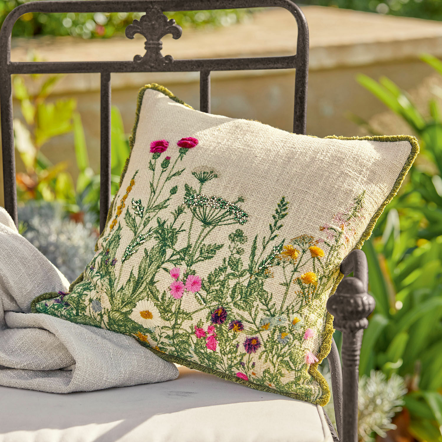 Kissenhülle Aranno Beiges Leinenkissen mit bunter Blumenstickerei und grünem Rand auf einem Metall-Gartenstuhl