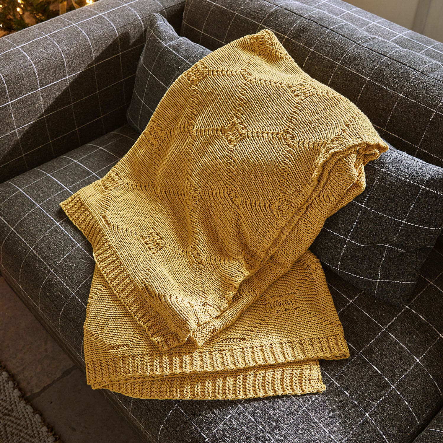 Plaid Cresil Gelbe gestrickte Decke mit geometrischem Muster auf grauem Karsofa drapiert