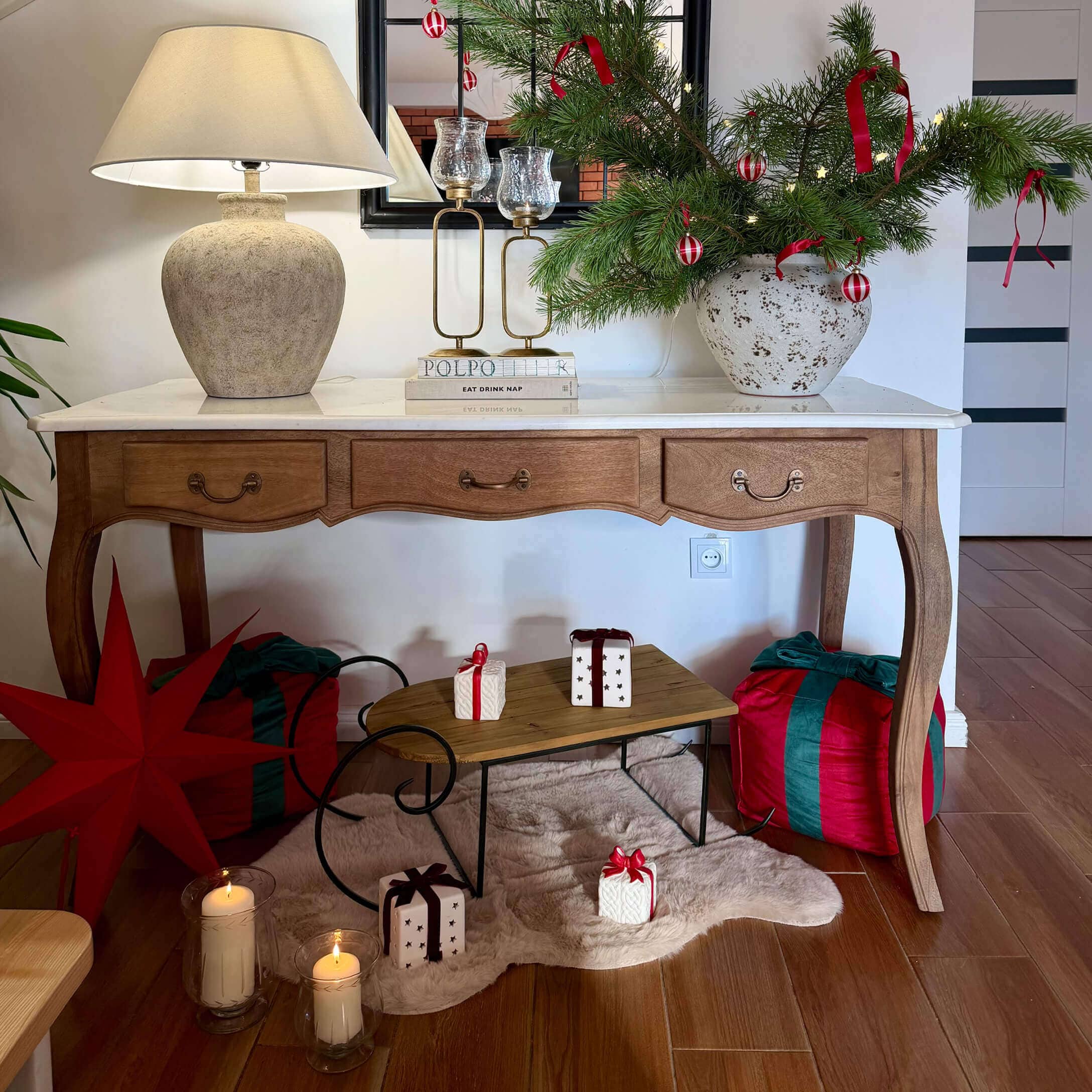 Holztisch mit weissem Tischblatt, Lampe und Weihnachtsdekoration aus grünen Zweigen mit roten Bändern