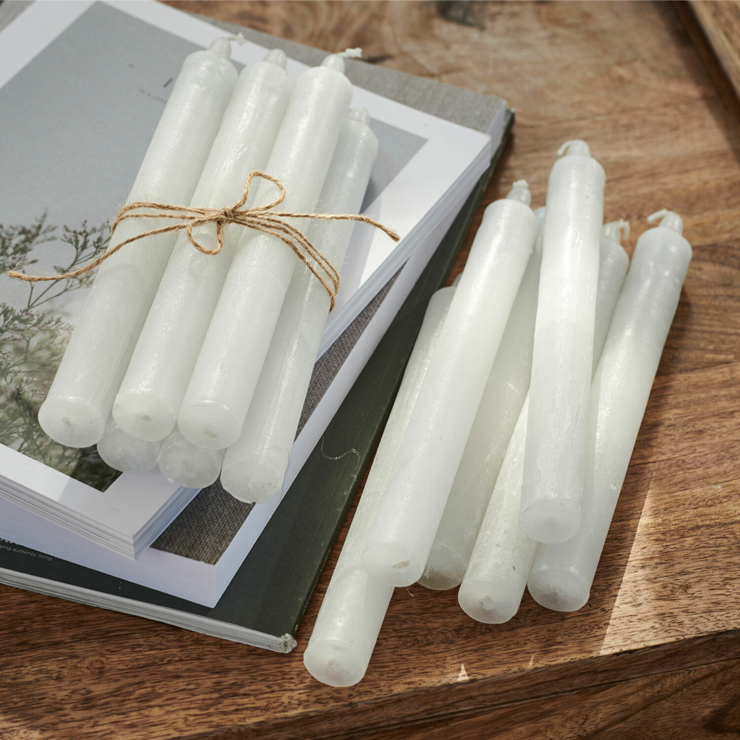 Kerze 12er Set Bauceau Set aus weissen Stabkerzen aus Wachs auf Holztisch mit Büchern, Wohnaccessoire