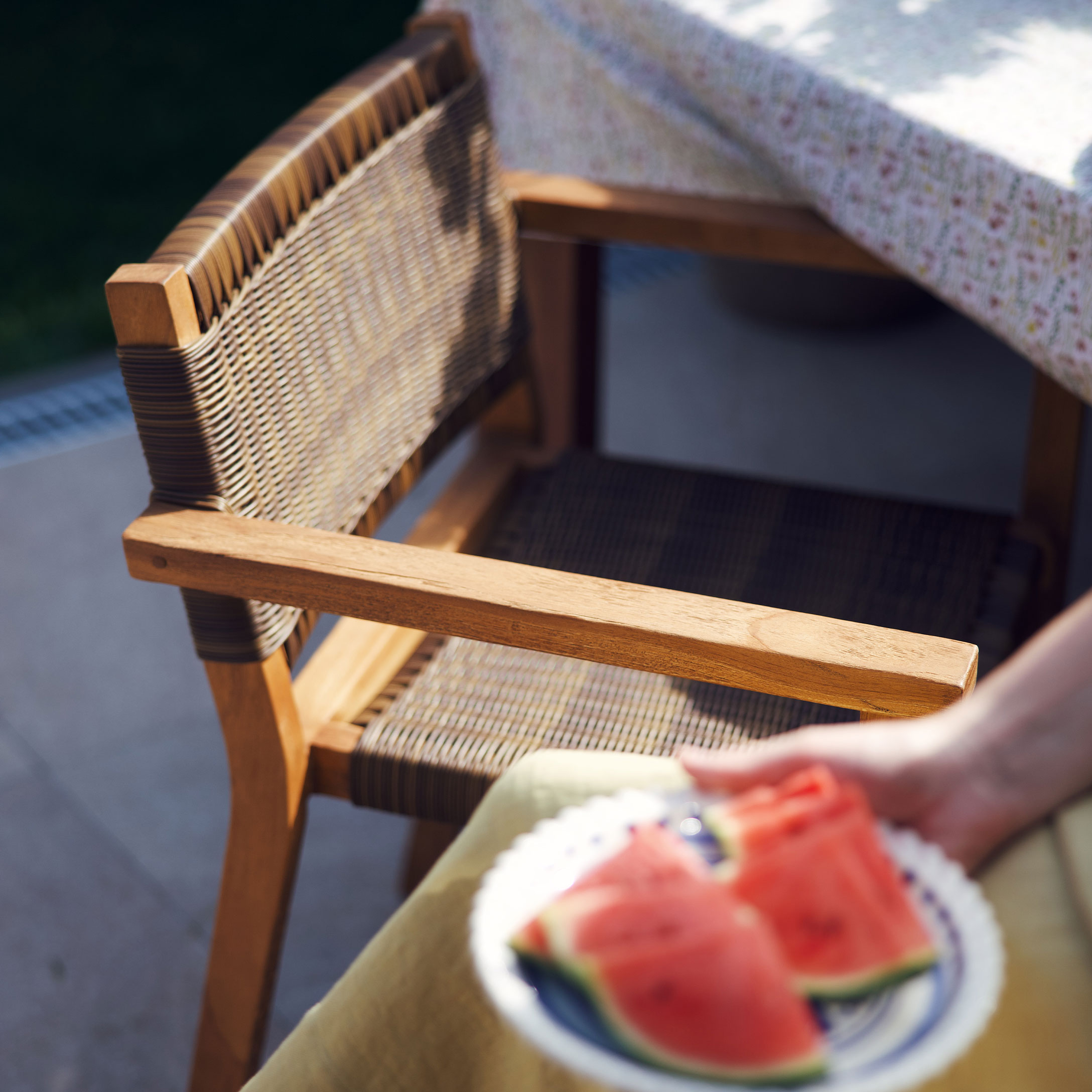 Gartenstuhl aus Holz und geflochtenem Material in Naturtönen neben einem Tisch mit Tischdecke