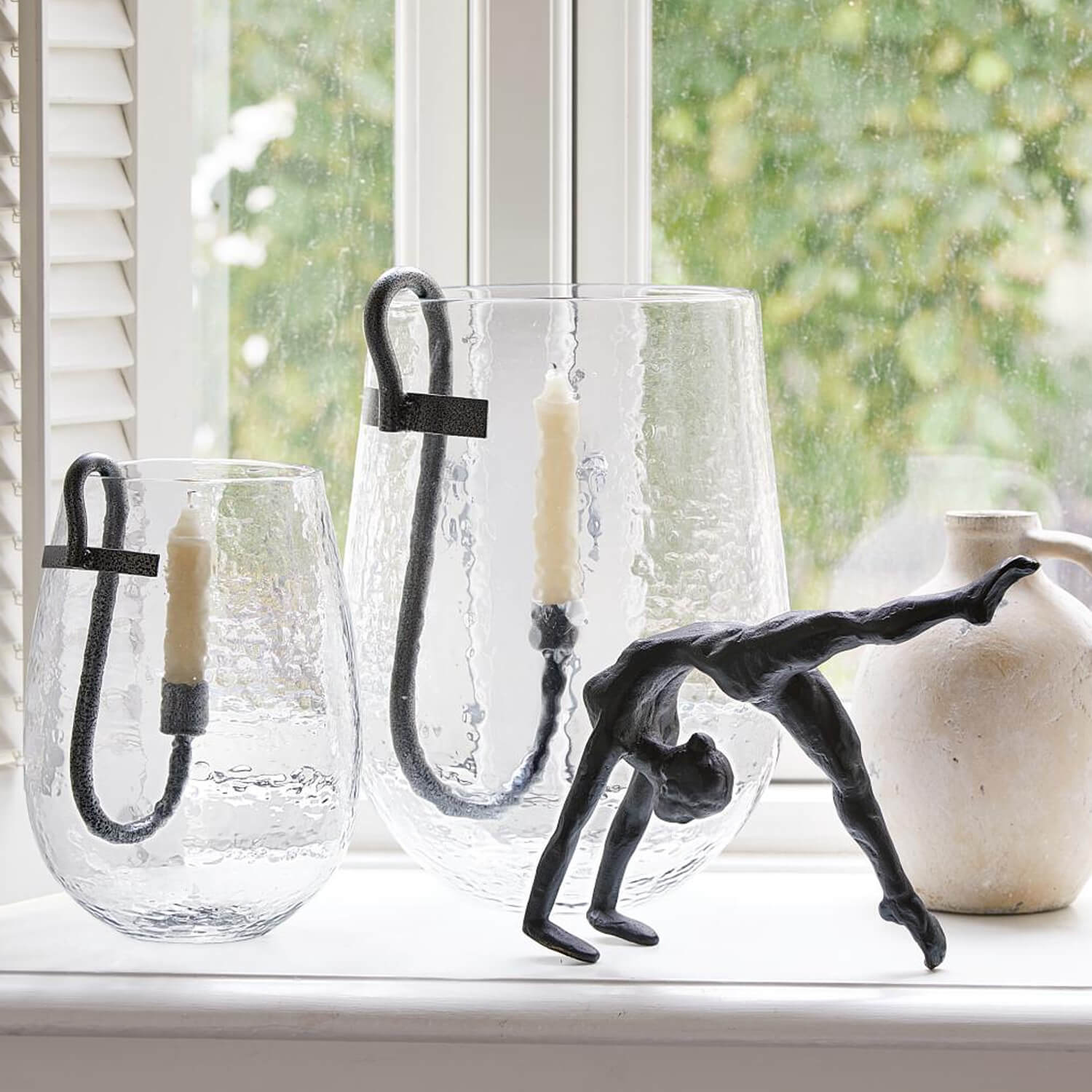 Glas-Kerzenhalter mit schwarzen Metallgriffen und weissen Kerzen, schwarze Tänzer-Skulptur auf Fensterbank