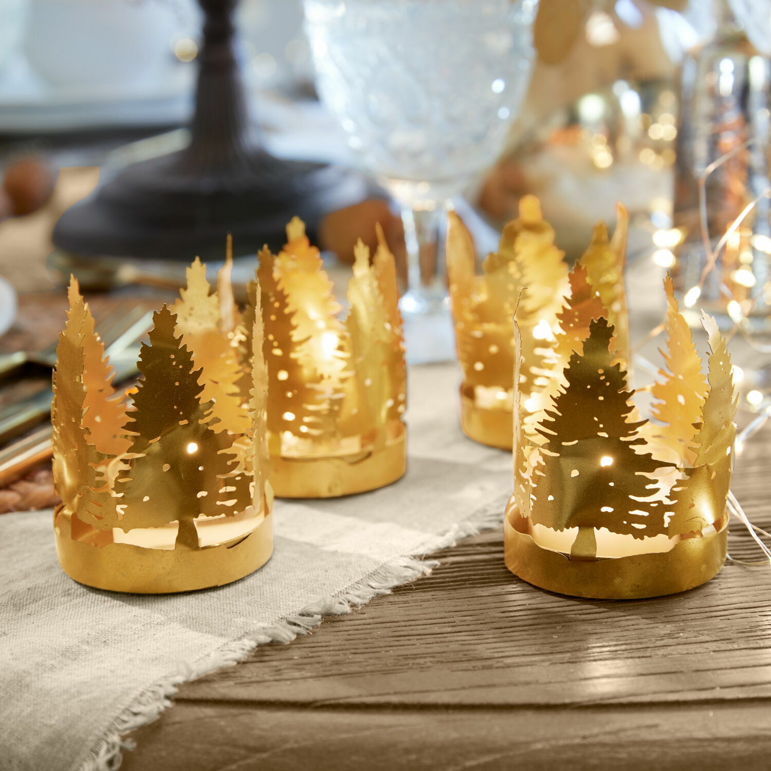Teelichthalter 4er Set Ismerie Goldene Metall-Teelichthalter mit Tannenbaum-Motiv auf Holztisch, festliche Dekoration