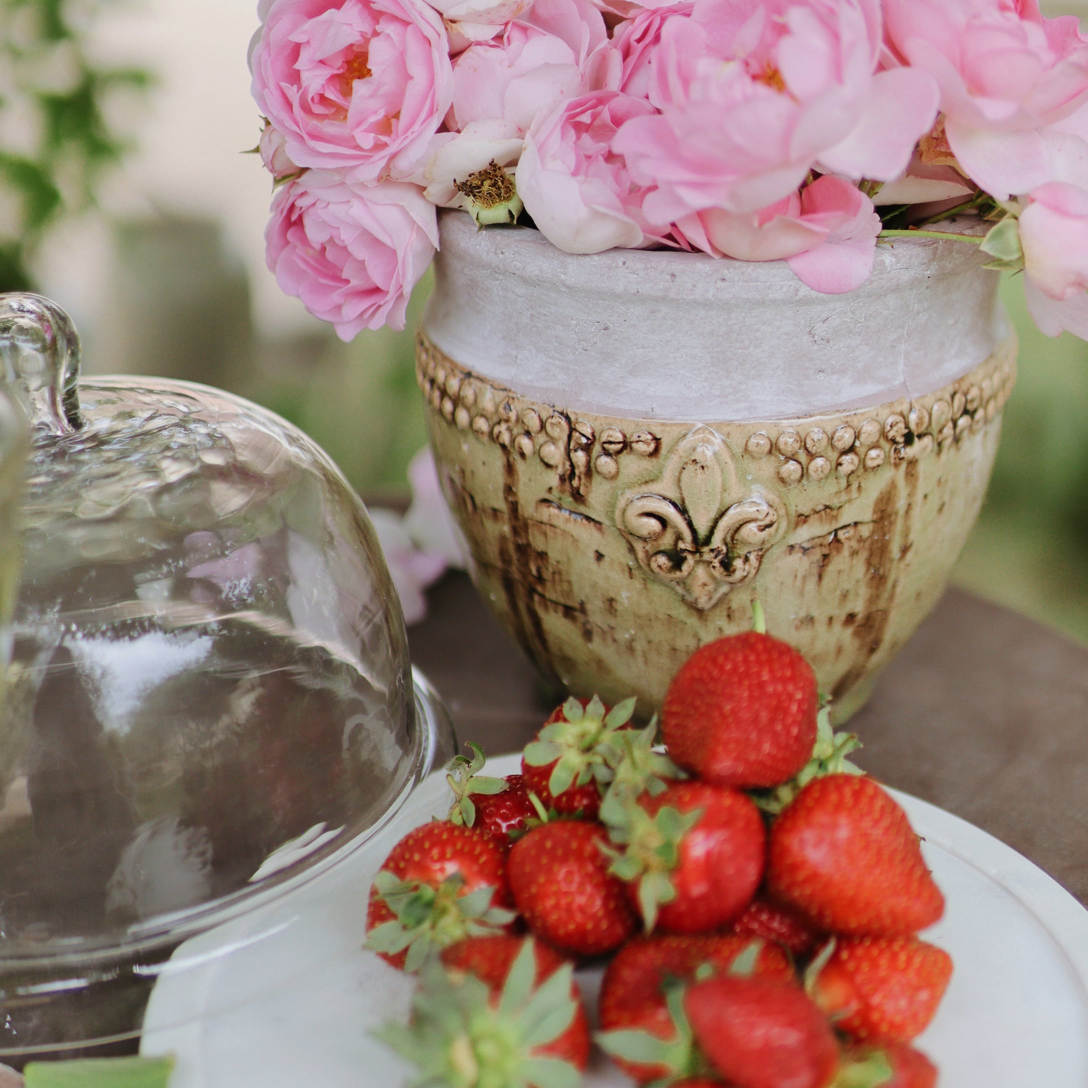 Keramiktopf mit rosa Blumen und frischen Erdbeeren auf weissem Teller