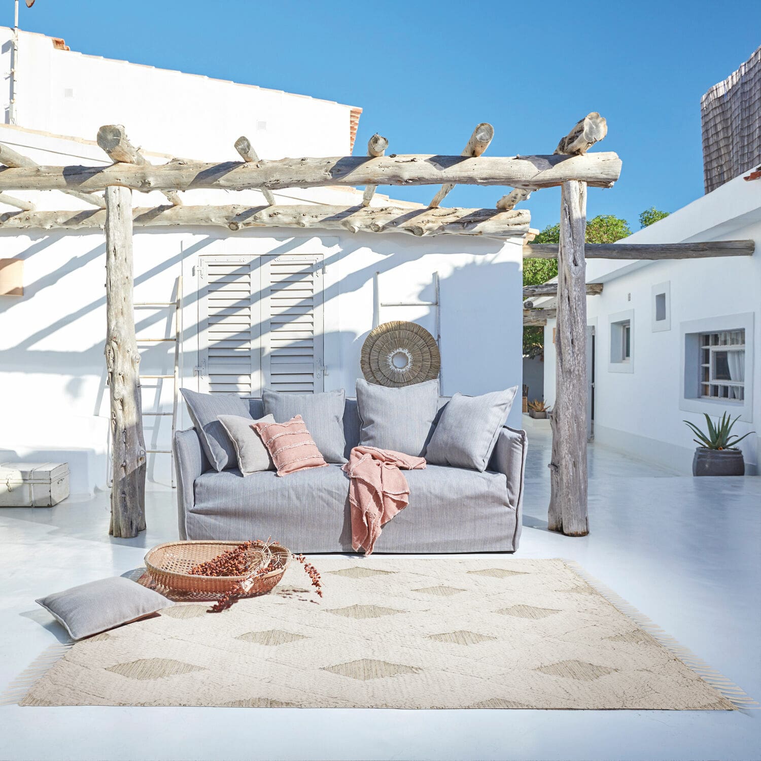 In- & Outdoor-Teppich Meagan Graues Stoffsofa auf der Terrasse mit Naturteppich und rosa Kissen für entspannte Aussenbereiche