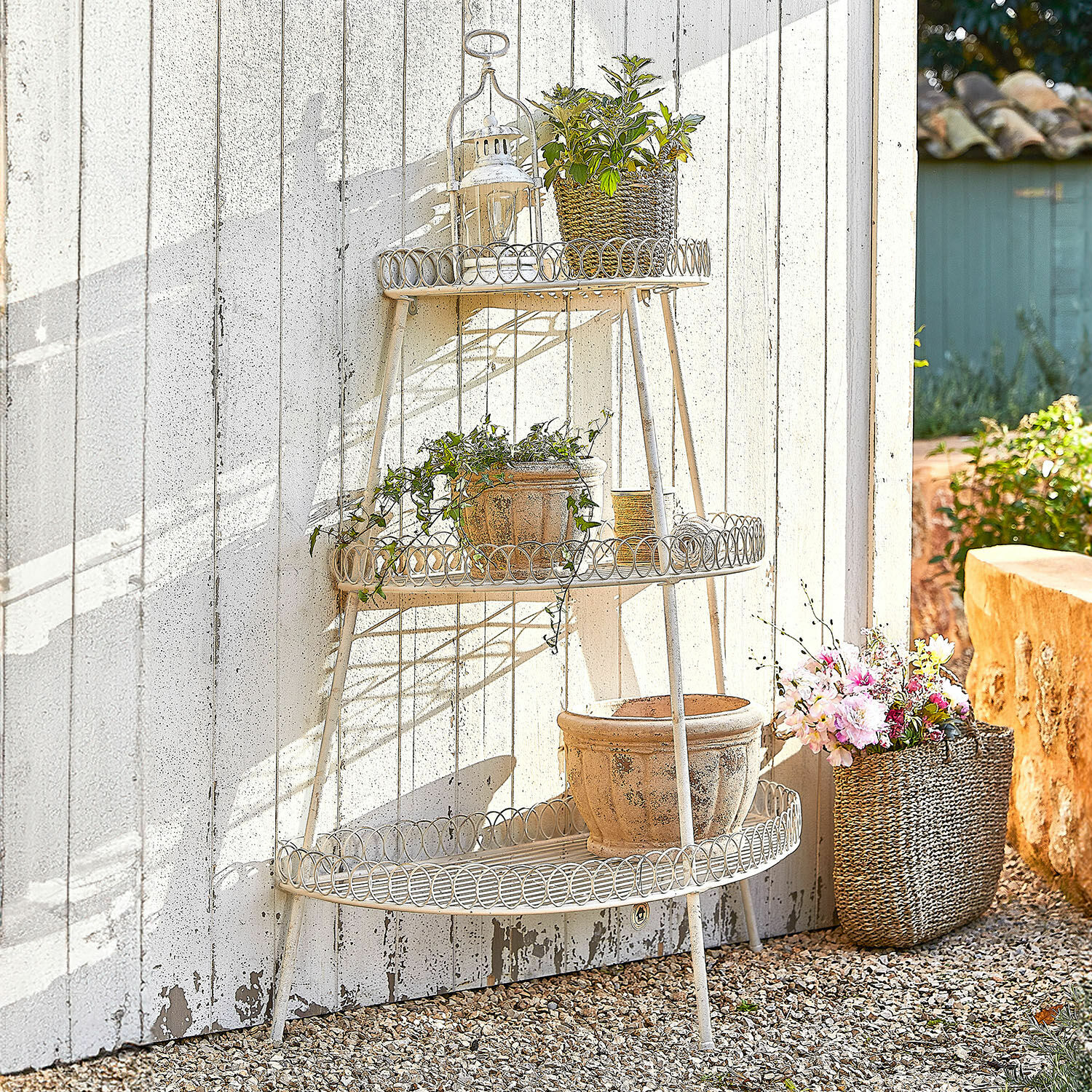 Etagere Lorivane Dreistufiges cremefarbenes Metallregal im Garten mit Blumentöpfen vor weisser Wand