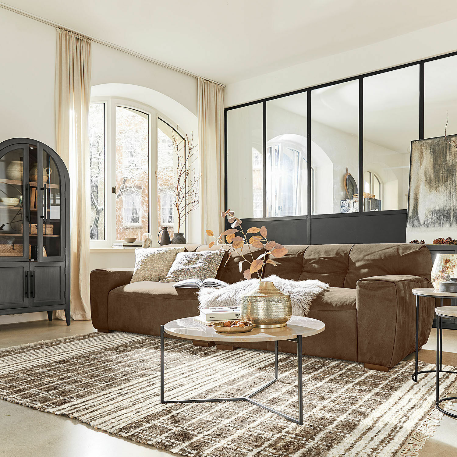 Teppich Berinique Braunes Mikrofaser-Sofa im hellen Wohnzimmer mit dekorativem Teppich und rundem Couchtisch