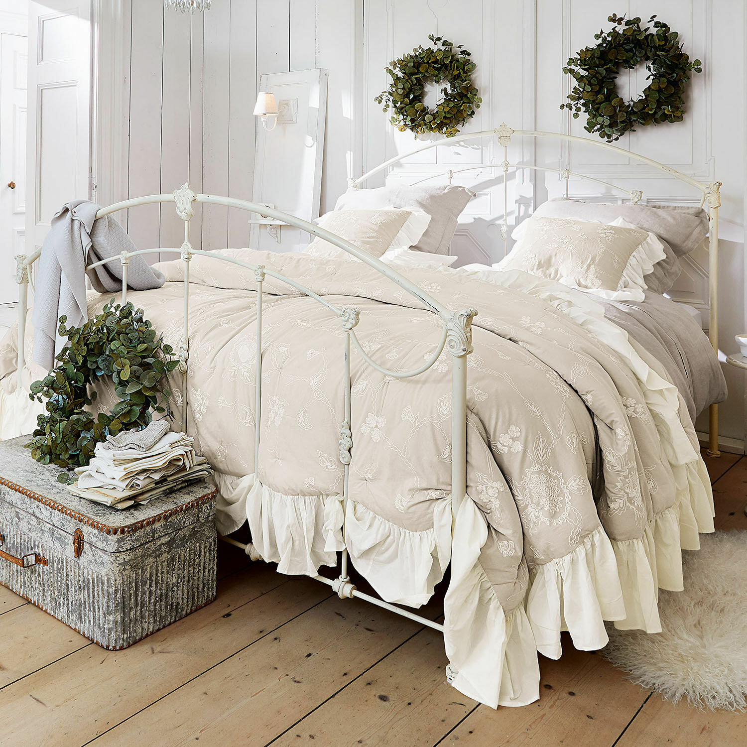 Quilt Clarissa Beige bestickte Bettwäsche mit Rüschen auf weissem Metallbett in hellem Schlafzimmer mit grünen Kränzen