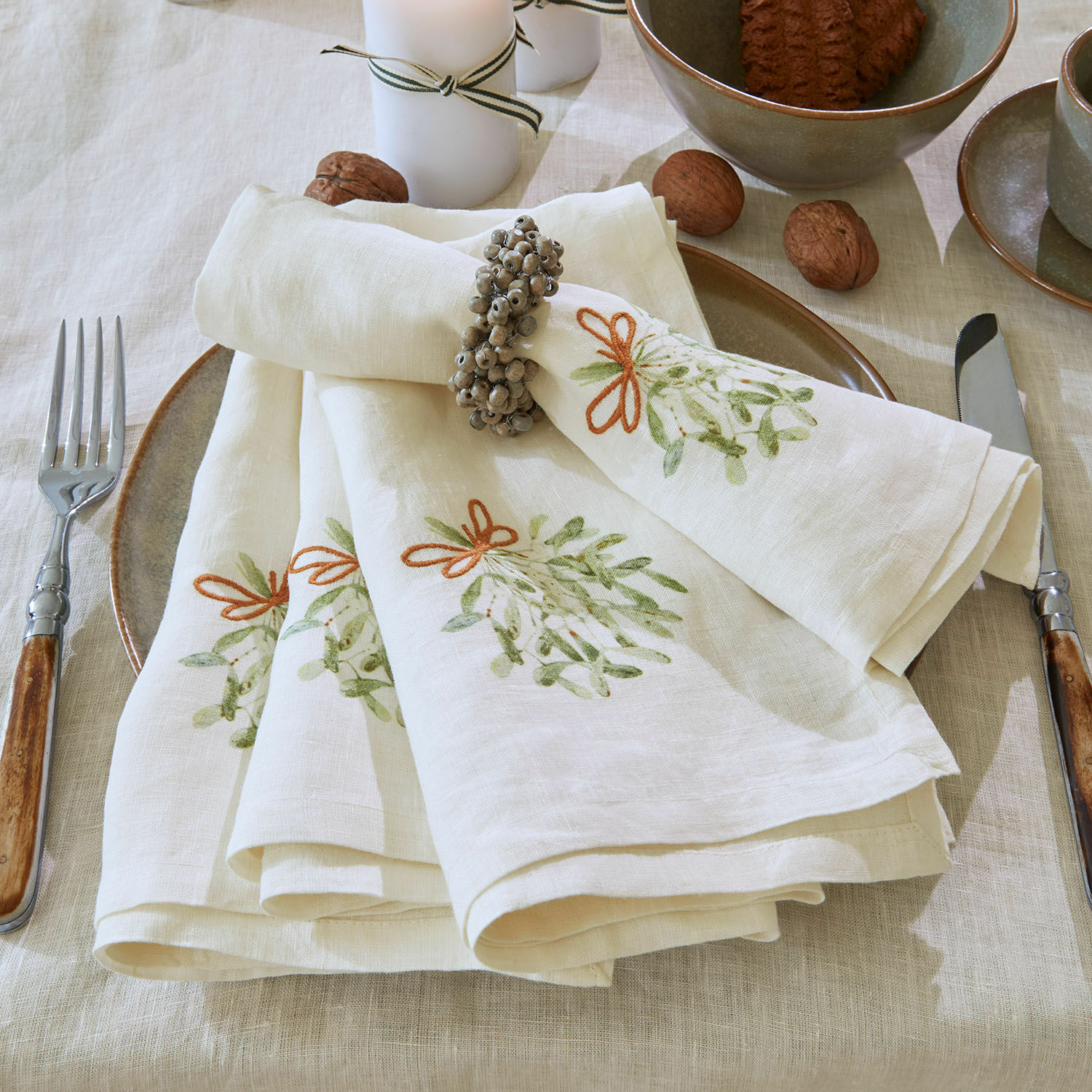Serviette 4er Set Mistletoe Leinenservietten in Creme mit grünem Muster und Serviettenring auf gedecktem Tisch mit Walnüssen
