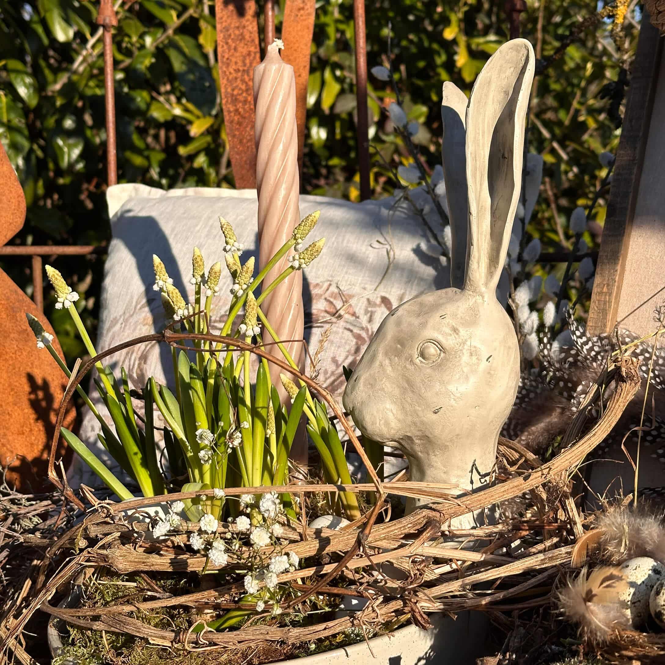Natürlich dekorierte Osterfreude mit grauem Keramikhasenkopf und grünen Blumen im Naturkorb.