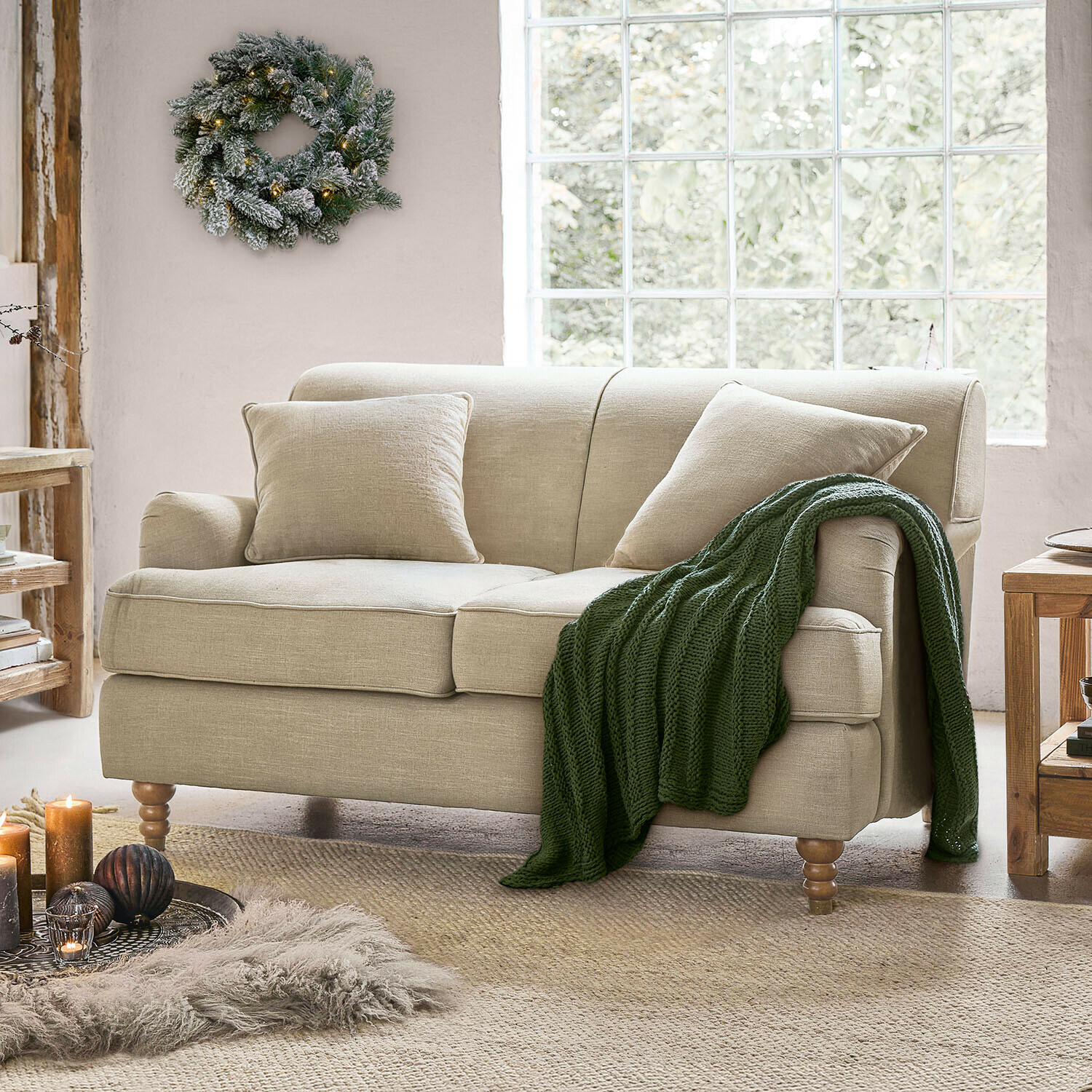 Sofa Isa Beiges Sofa aus Stoff mit Kissen und gestrickter Decke in hellem Wohnzimmer mit grossem Fenster