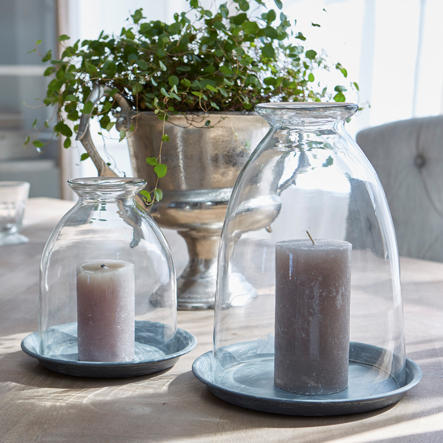 Grau Kerzen unter transparenten Glasglocken auf grauen Metallplatten auf einem Tisch