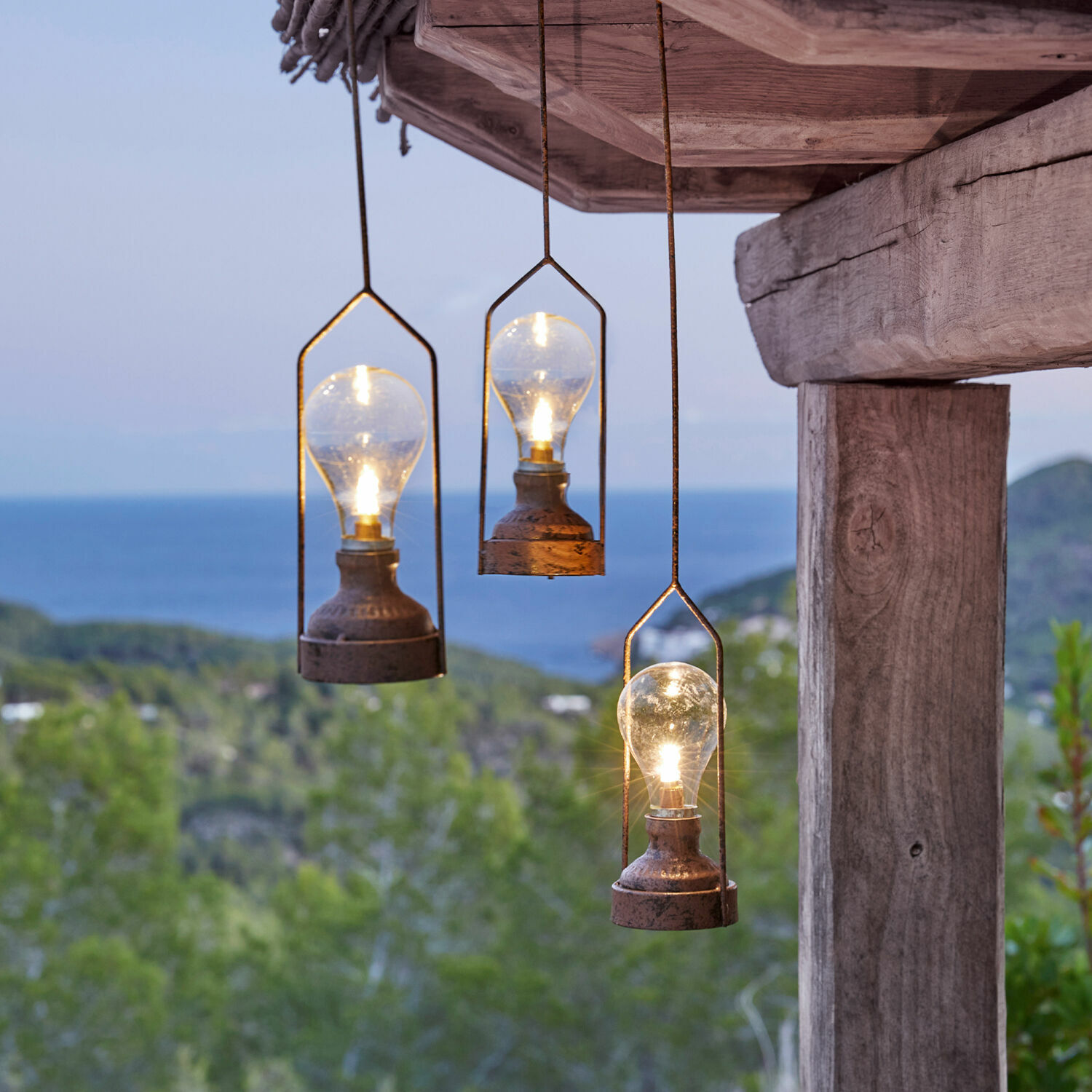 LED-Hängelaterne 3er Set Chambéry Drei hängende Metalllampen mit Glühbirnen vor grünem Wald und Meer, Aussenbeleuchtung