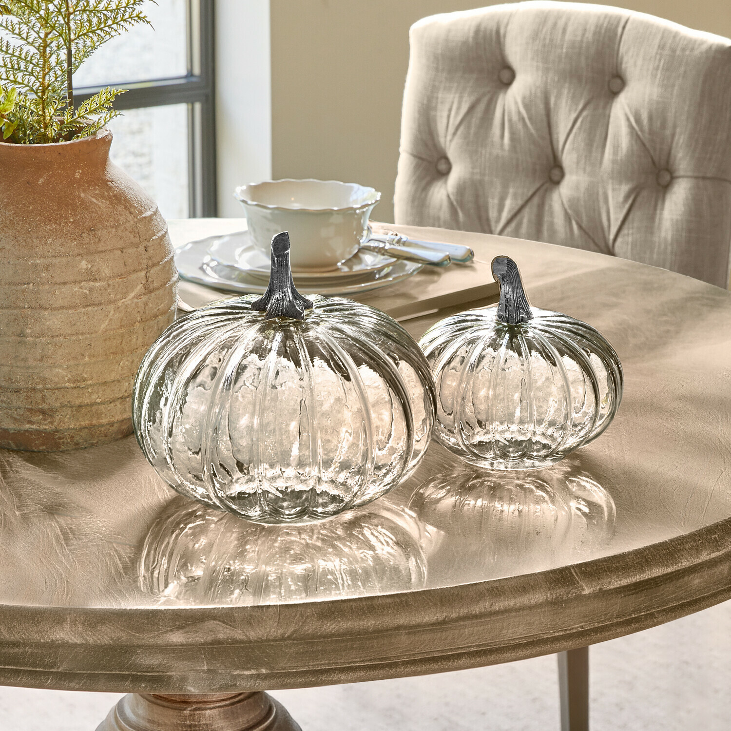 Kürbis 2er Set Perlouin Zwei transparente Glas-Kürbisse mit Metallstielen auf einem beigen Dekotisch