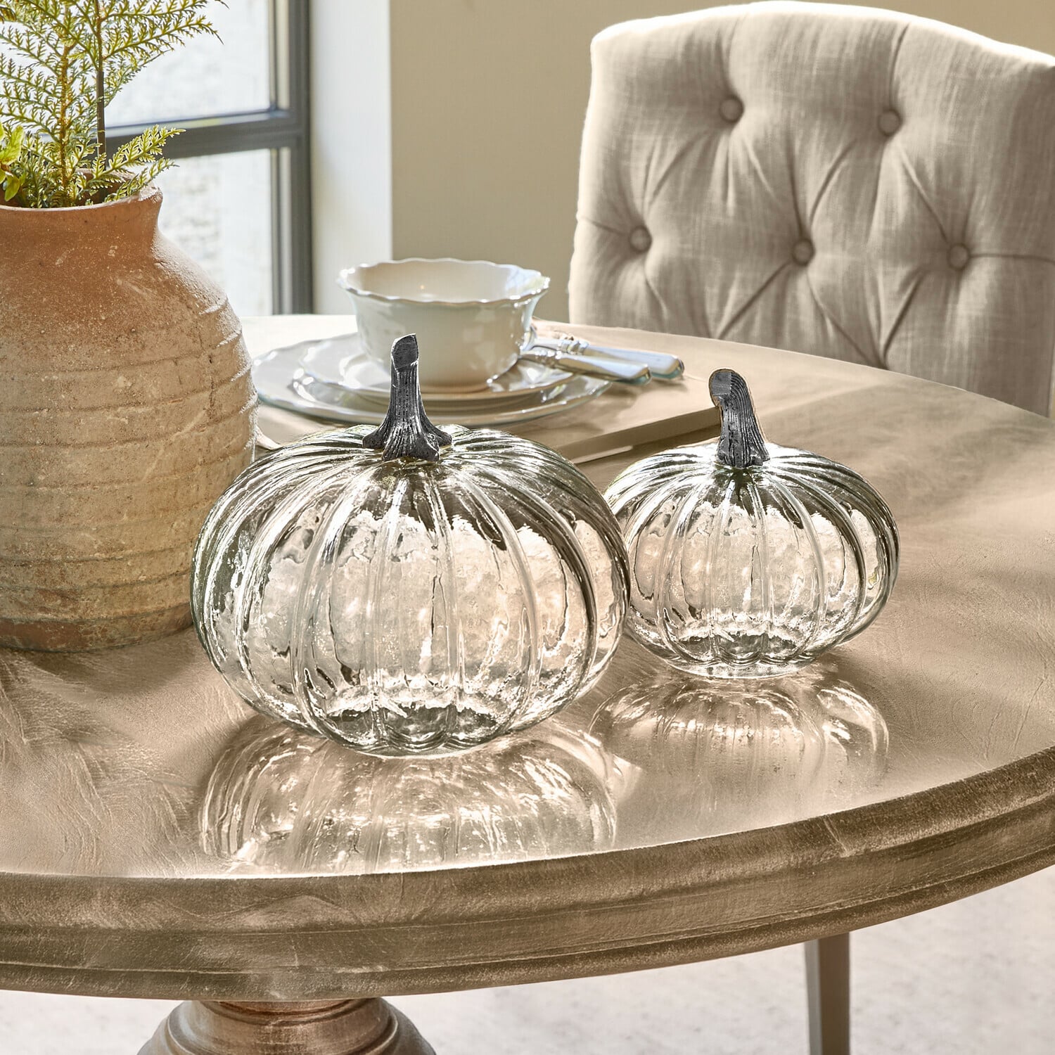 Kürbis 2er Set Perlouin Zwei transparente Glas-Kürbisse mit Metallstielen auf einem beigen Dekotisch