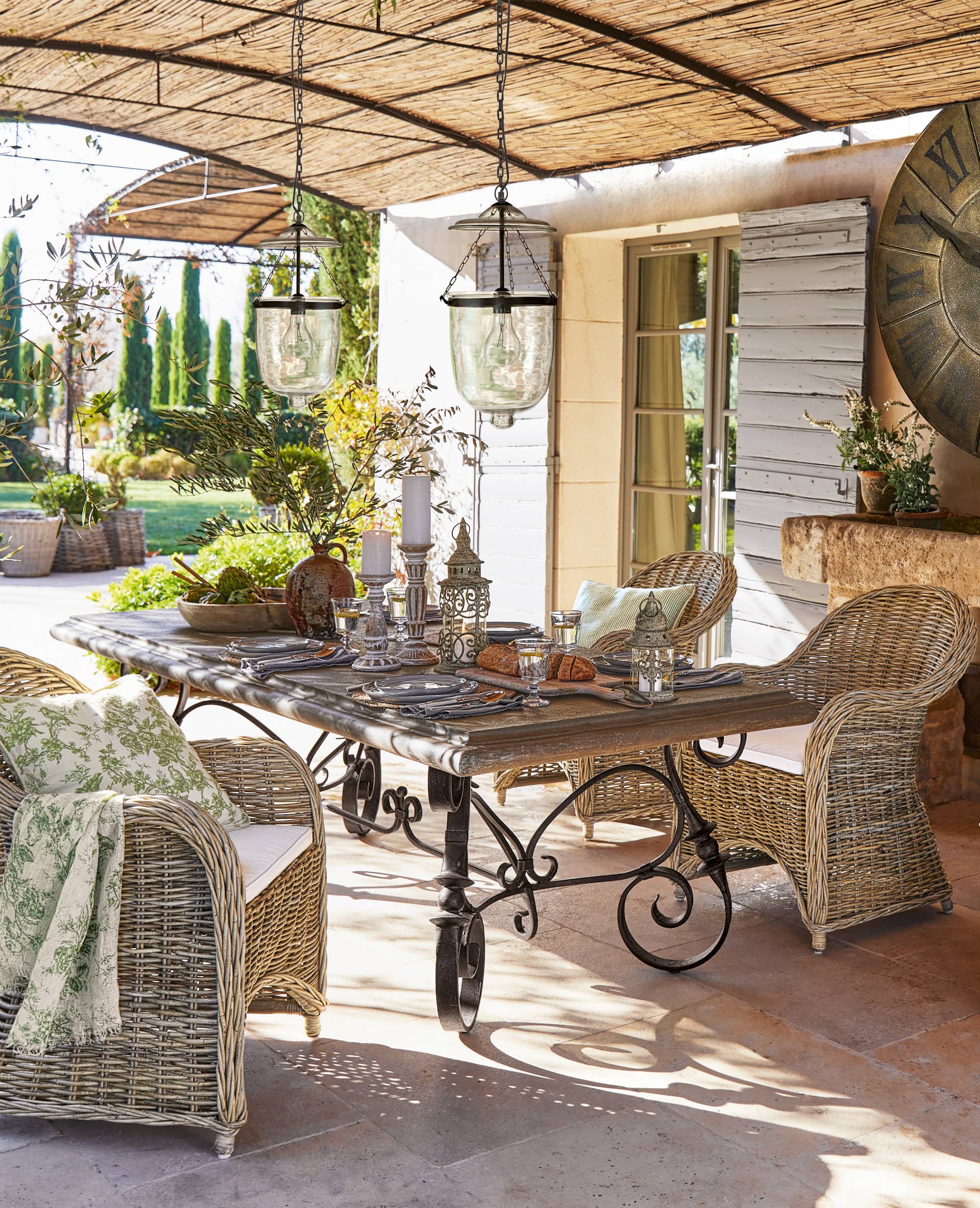 Rustikaler Gartentisch mit Eisenbeinen und Rattanstühlen auf der Terrasse mit hängenden Lampen