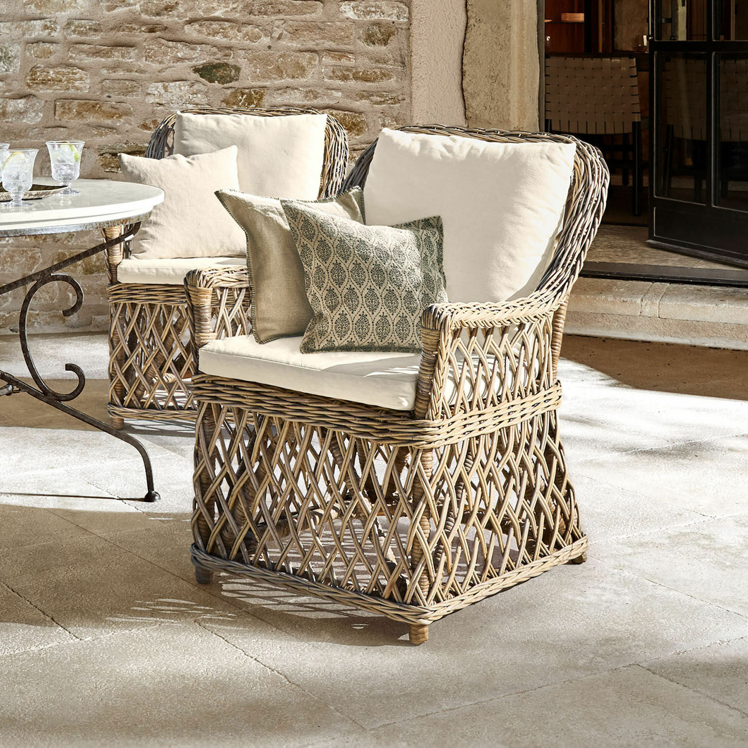 Sessel Nesvryn Bequemer Sessel aus natürlichem Rattan mit cremefarbenen Polstern und dekorativen Kissen für die Terrasse.