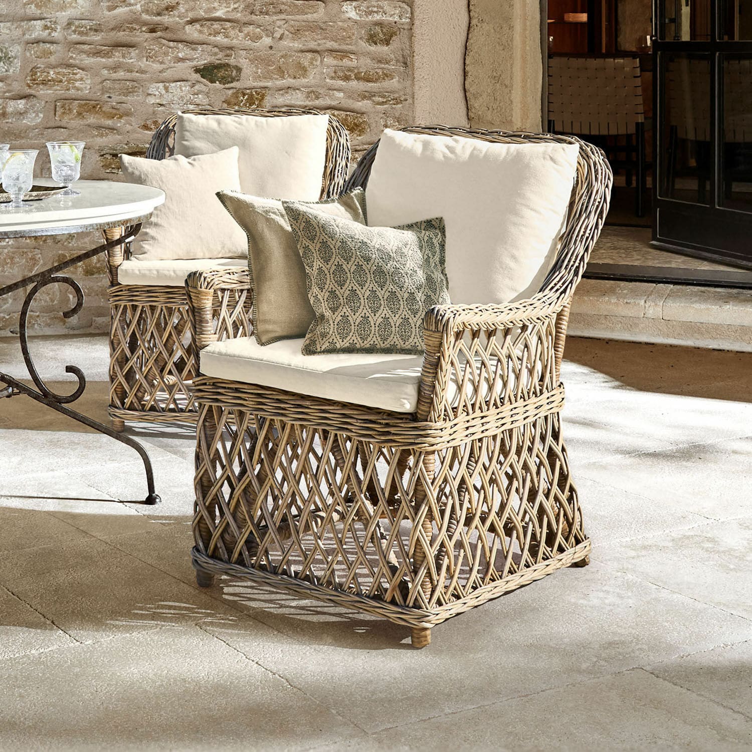 Sessel Nesvryn Bequemer Sessel aus natürlichem Rattan mit cremefarbenen Polstern und dekorativen Kissen für die Terrasse.