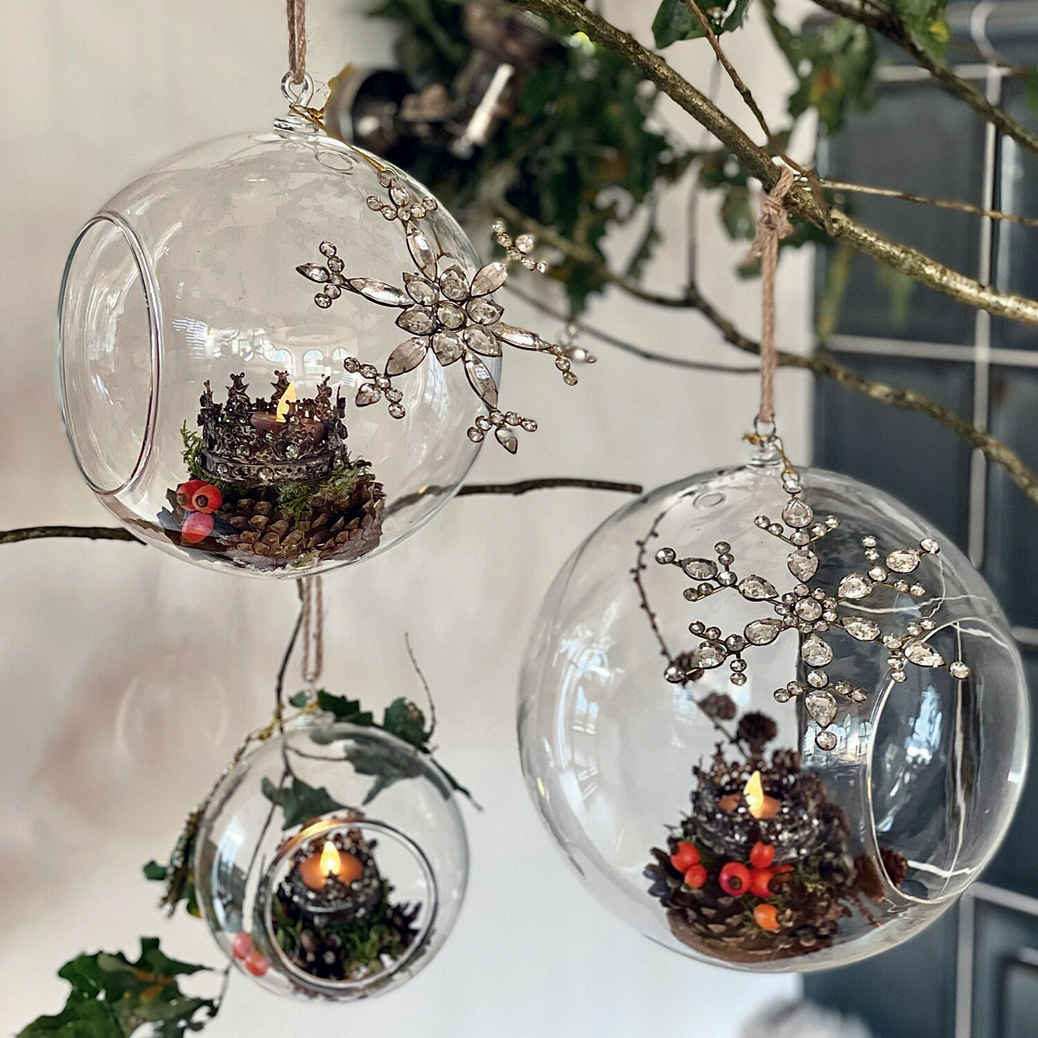 Glaskugeln mit Schneeflockenanhängern und Kerzen im Inneren, an Zweigen hängend, Weihnachtsdekoration