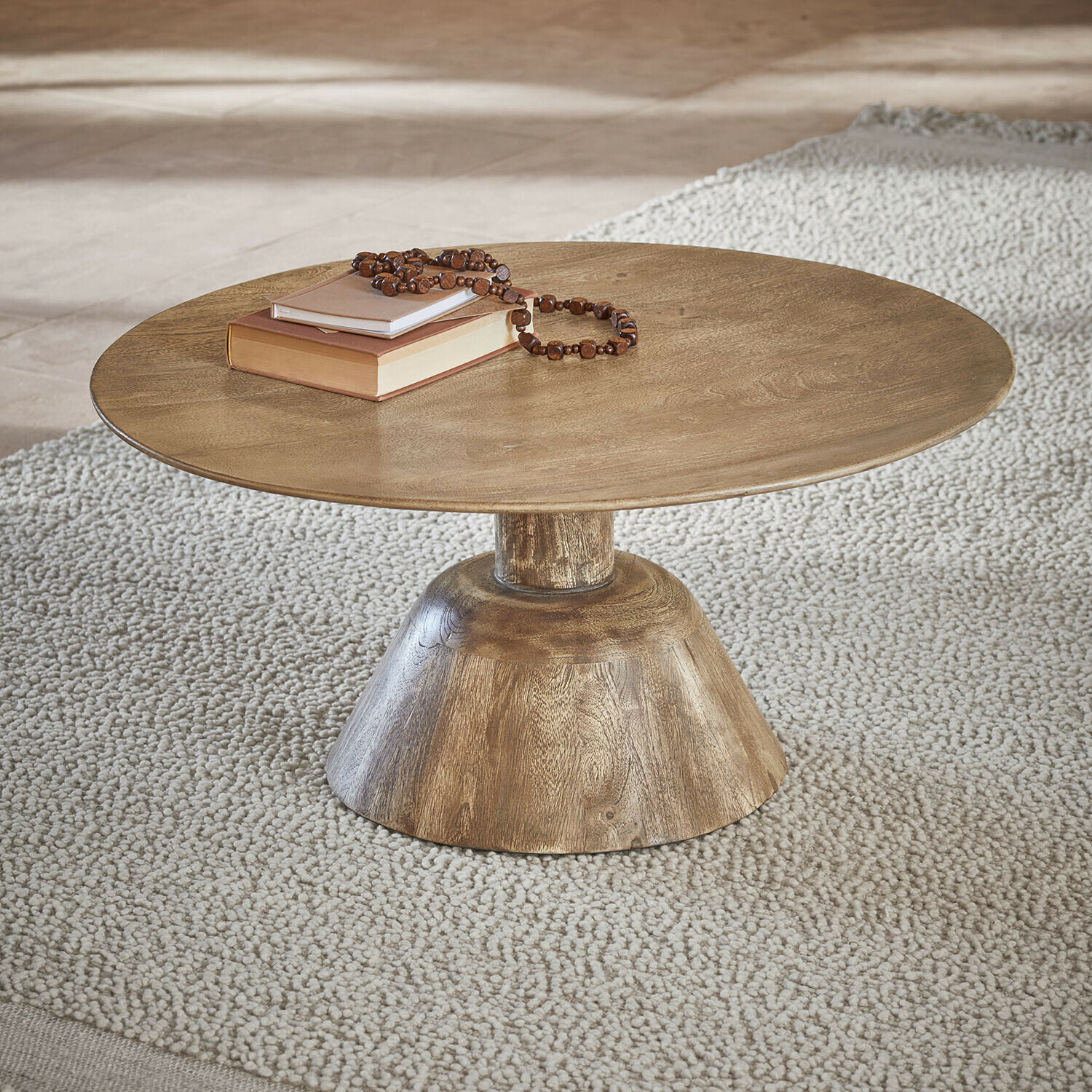 Runder Couchtisch aus Holz in Naturfarbe auf hellem Teppich mit Büchern und Perlenkette