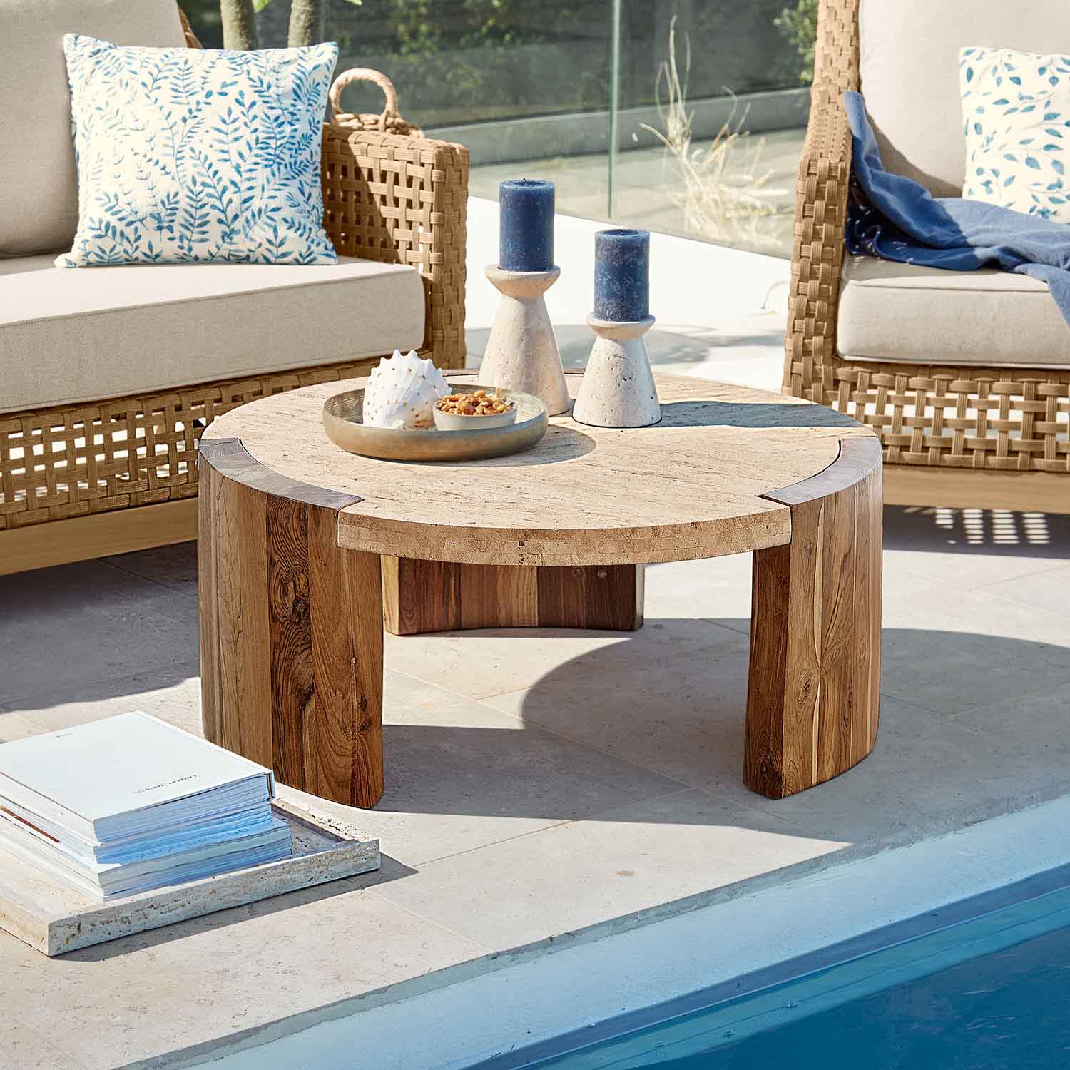 Runder Couchtisch aus hellem Holz und Stein auf Terrasse am Pool mit Kissen und Dekorationen