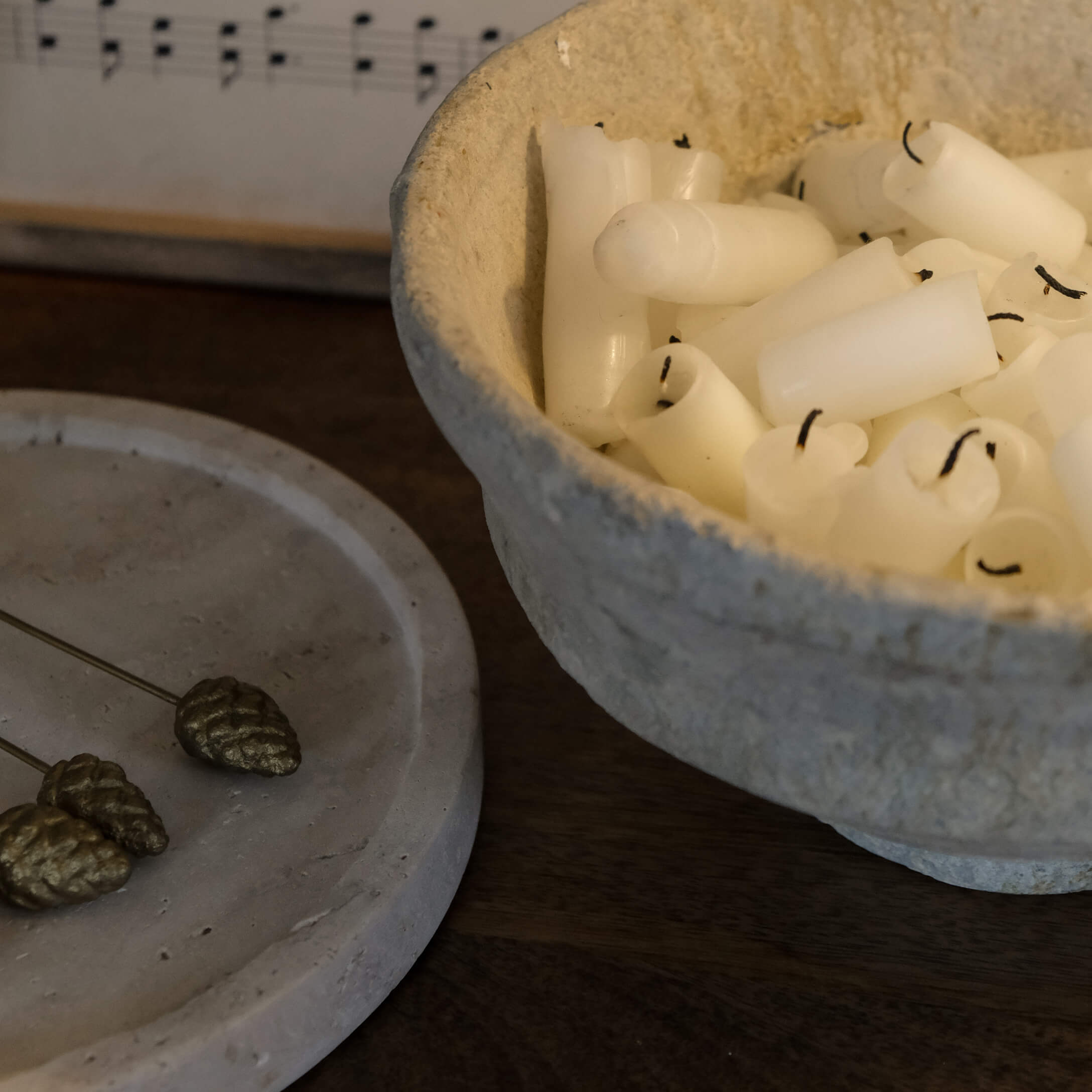 Schale aus Naturmaterial mit weissen Kerzen auf dunklem Holztisch, stimmige Dekoration