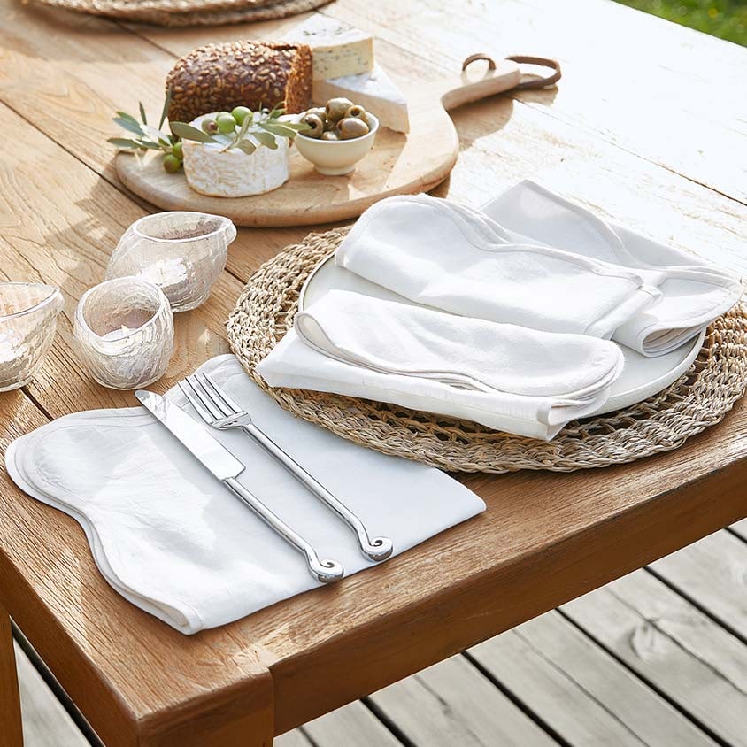 Weisses Leinen-Tischset mit Servietten und versilbertem Besteck auf Holztisch mit Snacks