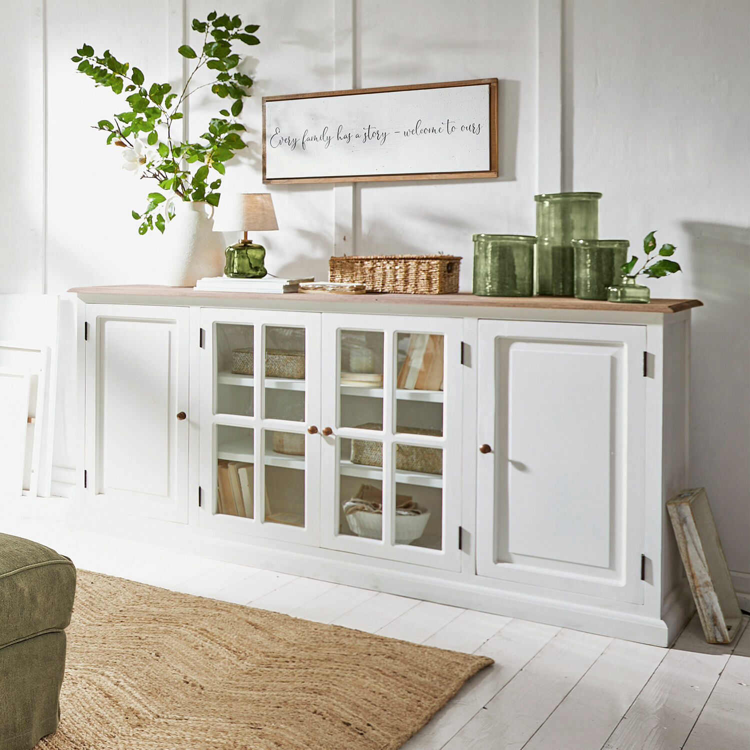 Kommode Kostan Weisse Holzkommode mit Glastüren und heller Holzplatte in einem hellen Wohnzimmer