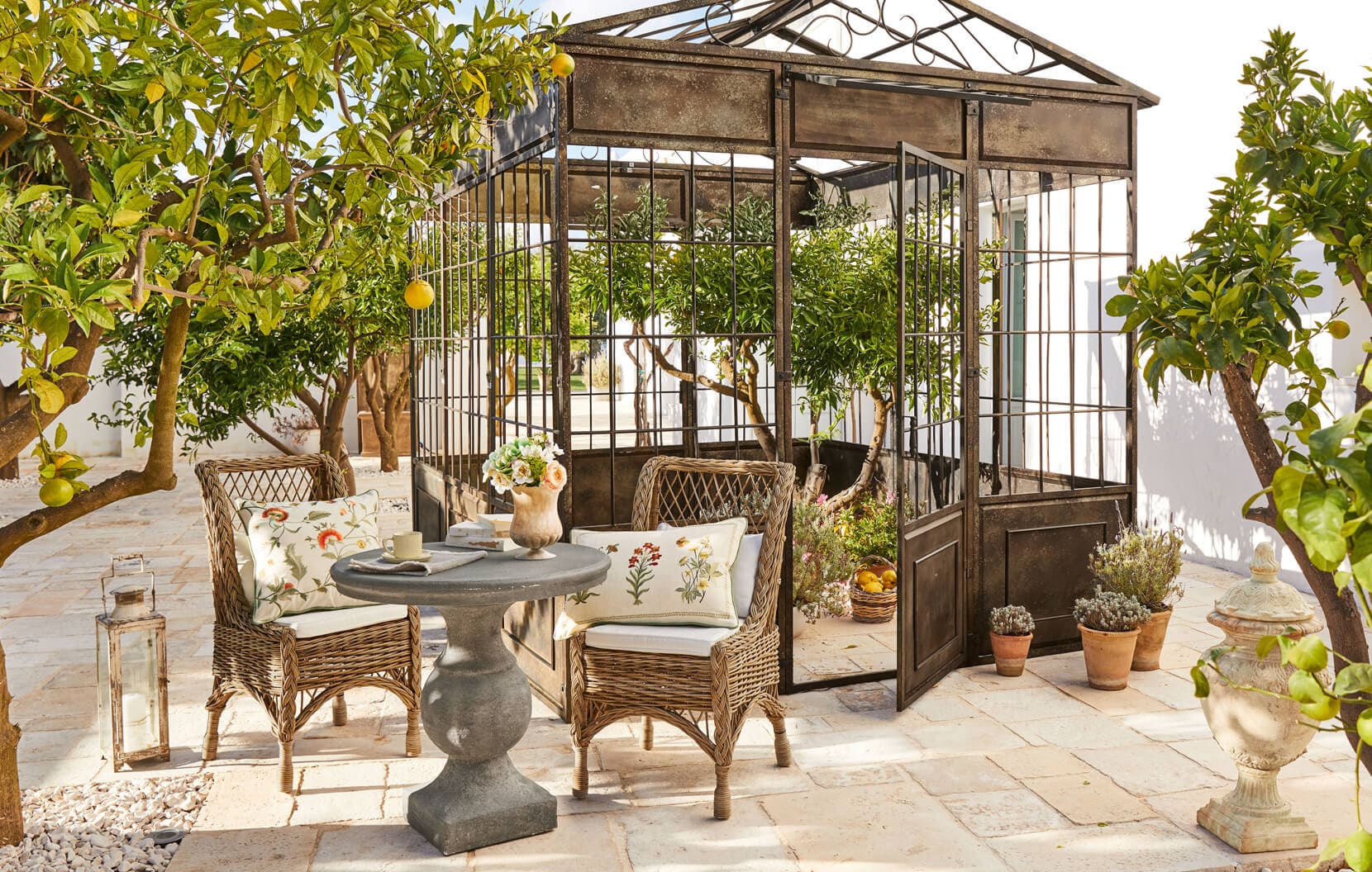 Mittelmeerlicher Garten mit Metallpavillon, Rattanstühlen und Steintisch auf der Terrasse
