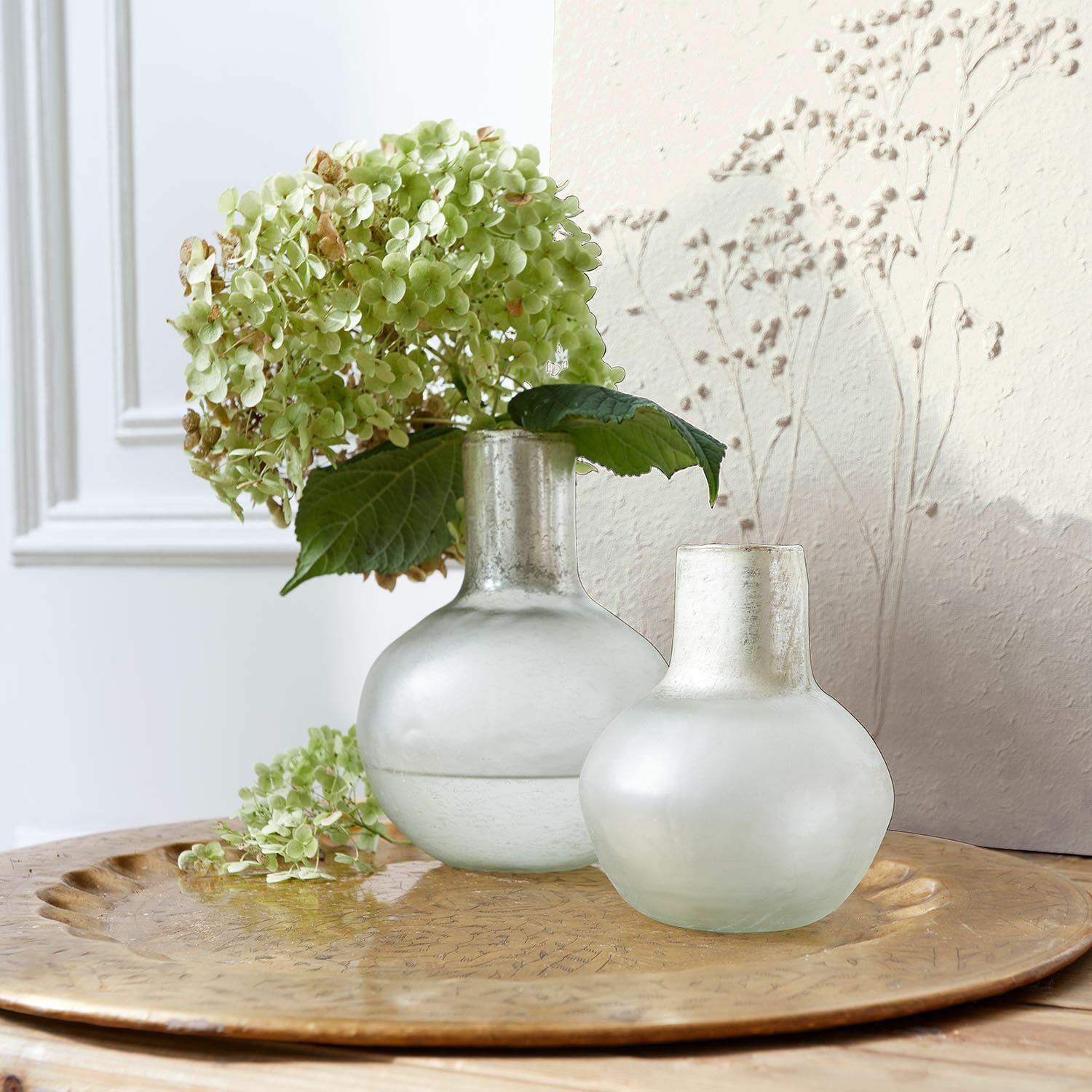 Vase 2er Set Nazira Zwei matte, milchglasfarbene Vasen auf einem goldfarbenen Tablett mit grünen Hortensienblüten