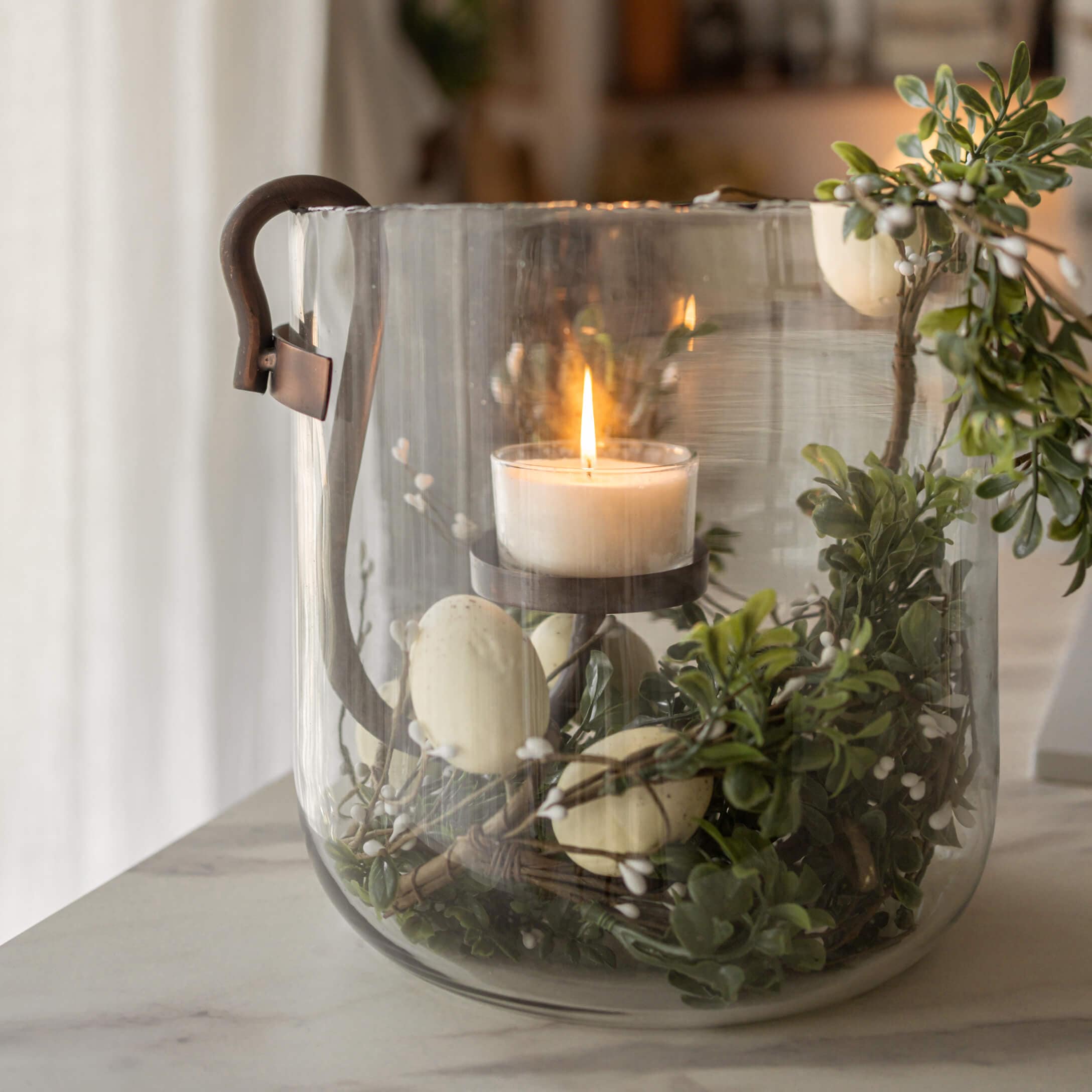 Glaslaterne mit Metallgriff, brennende weisse Kerze und grüne Blattdekoration mit weissen Beeren